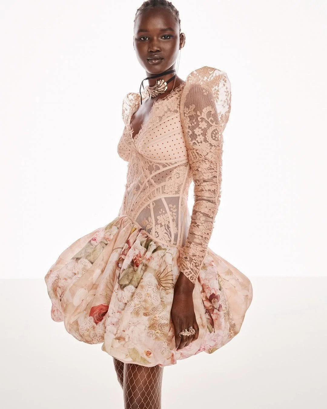Model wearing a pink lace and floral dress with puffed skirt, standing against a white background.