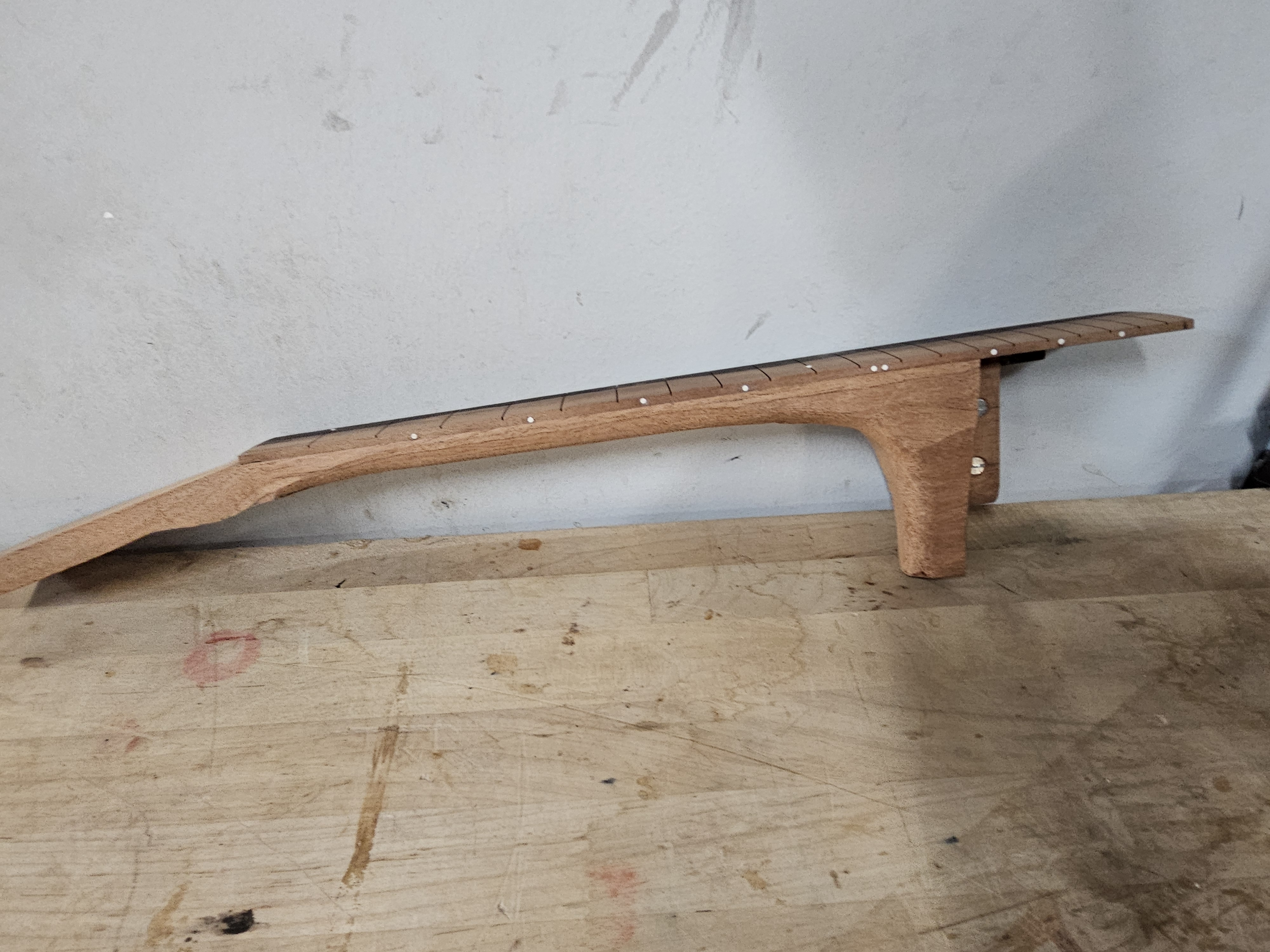A wooden skateboard ramp with a curved incline and a small vertical section, placed on a rustic wooden table against a plain wall.