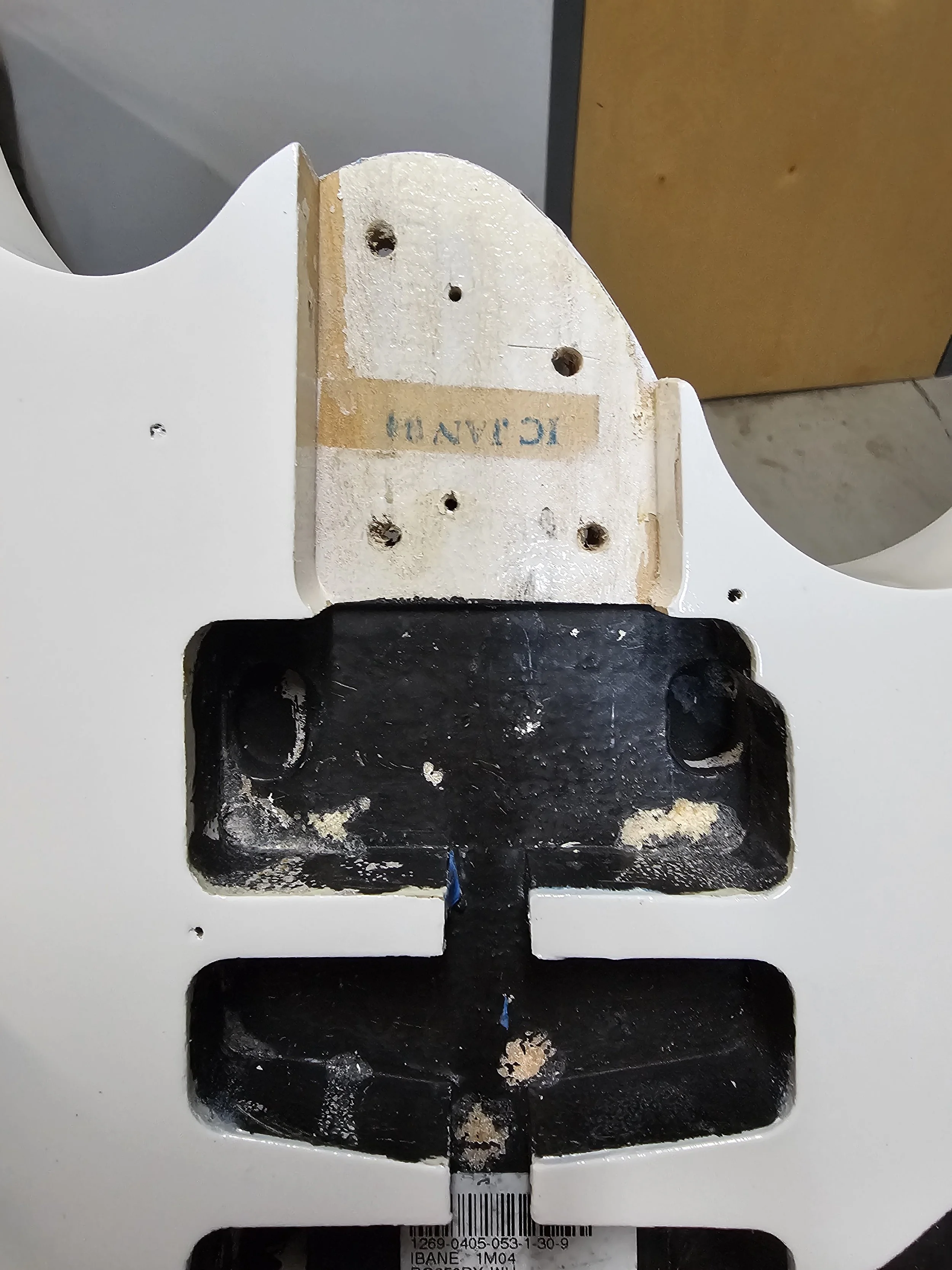 View of the underside of a white wooden furniture piece with mounting holes and a black mounting bracket.