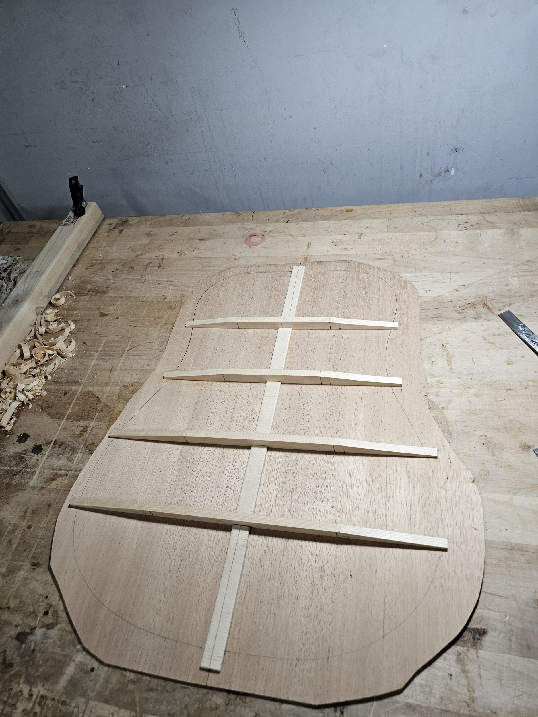 Unfinished wooden guitar body with braces on a woodworking table.