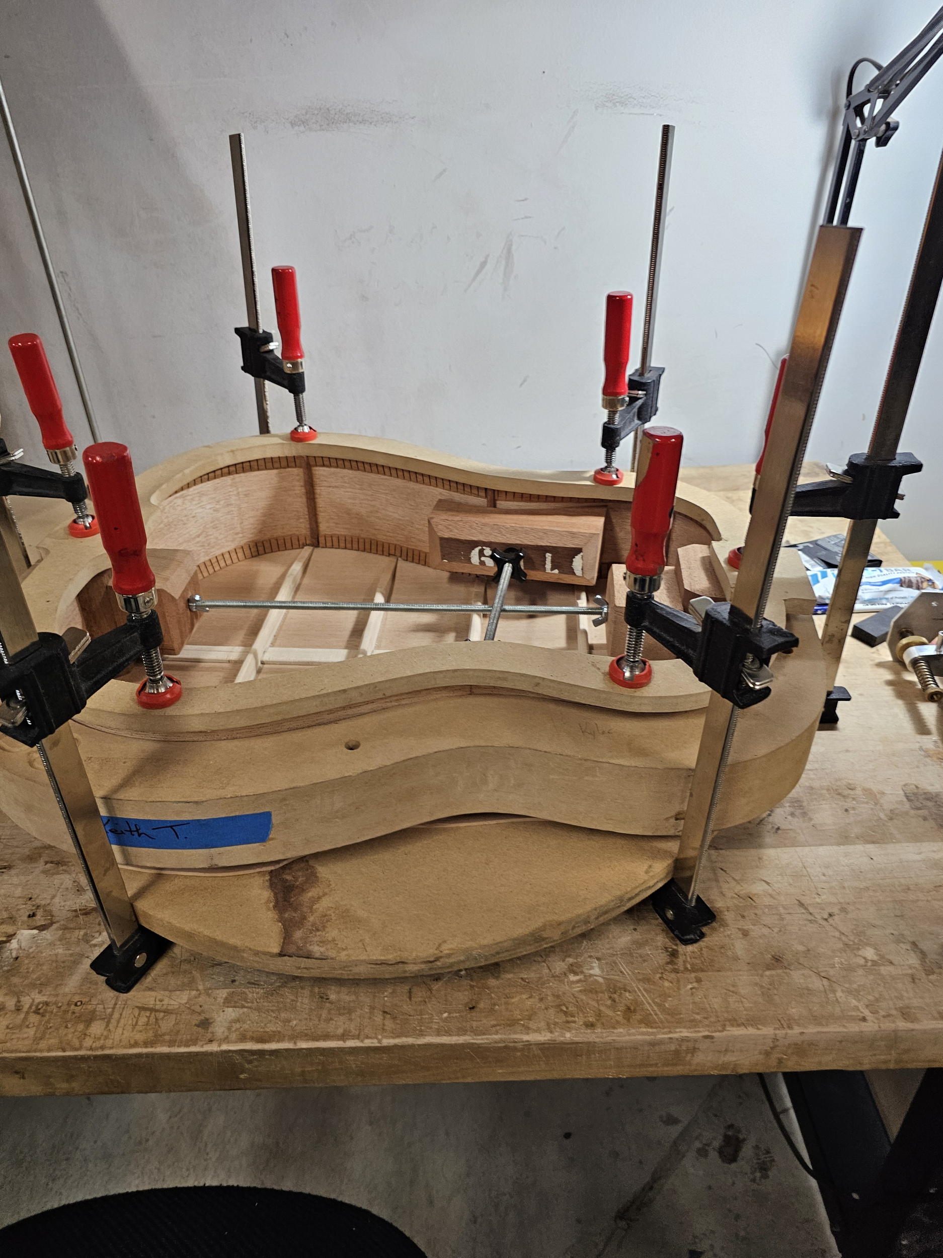 Woodworking project in progress with multiple clamps holding pieces of wood together on a workbench.