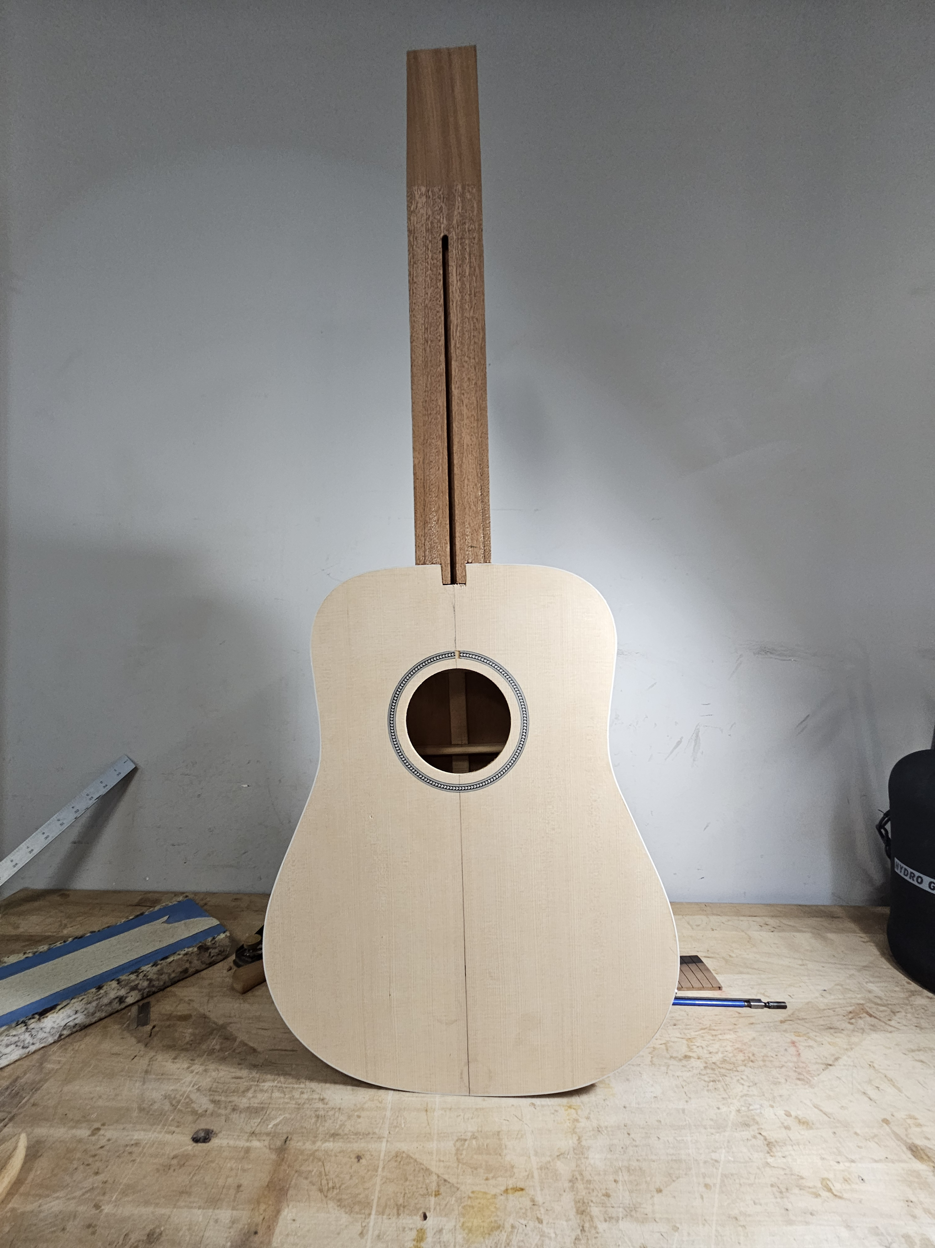 An unfinished acoustic guitar on a workbench in a woodworking shop.