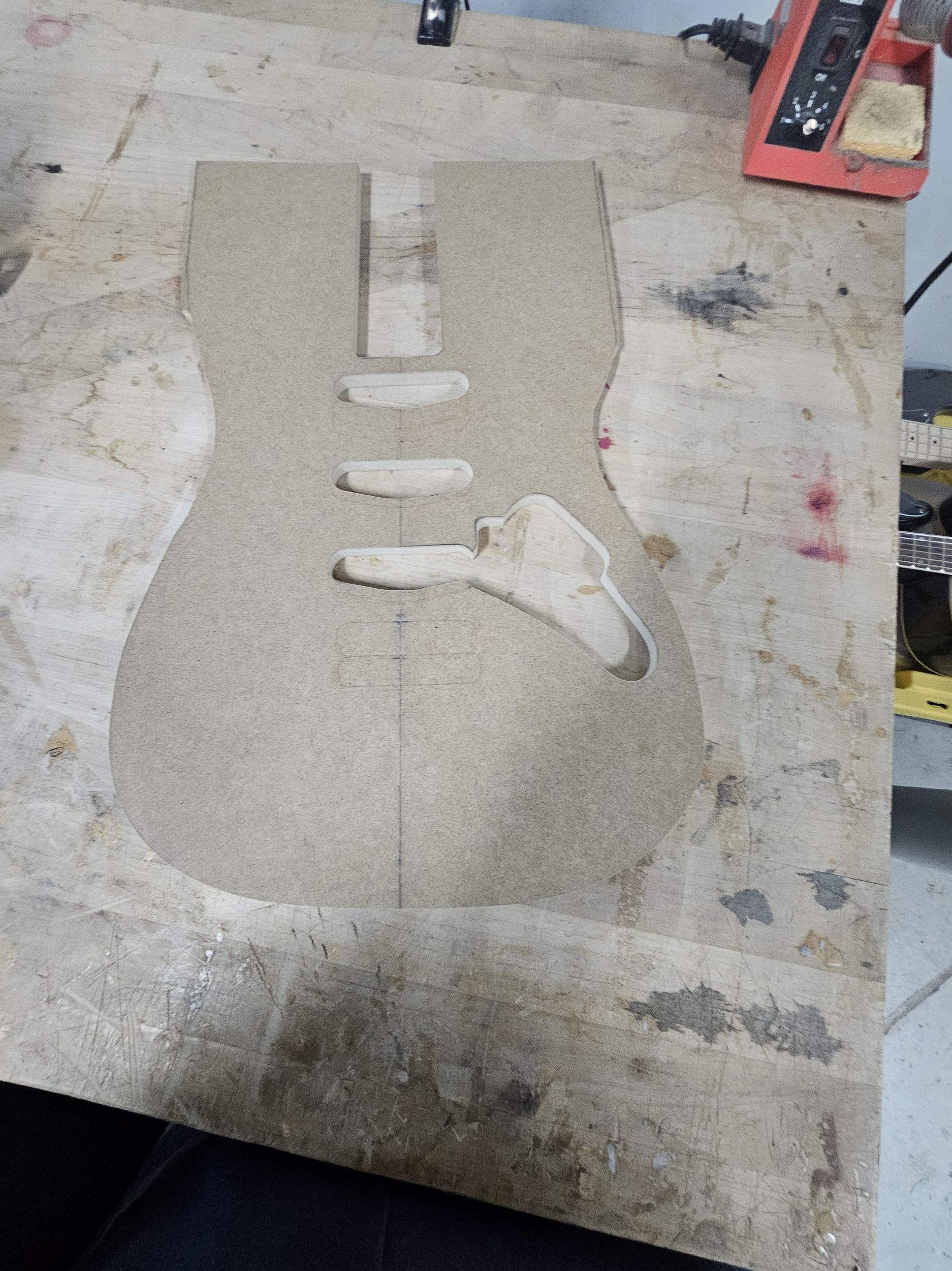 Wooden guitar-shaped template with cutouts and slots on a workbench.