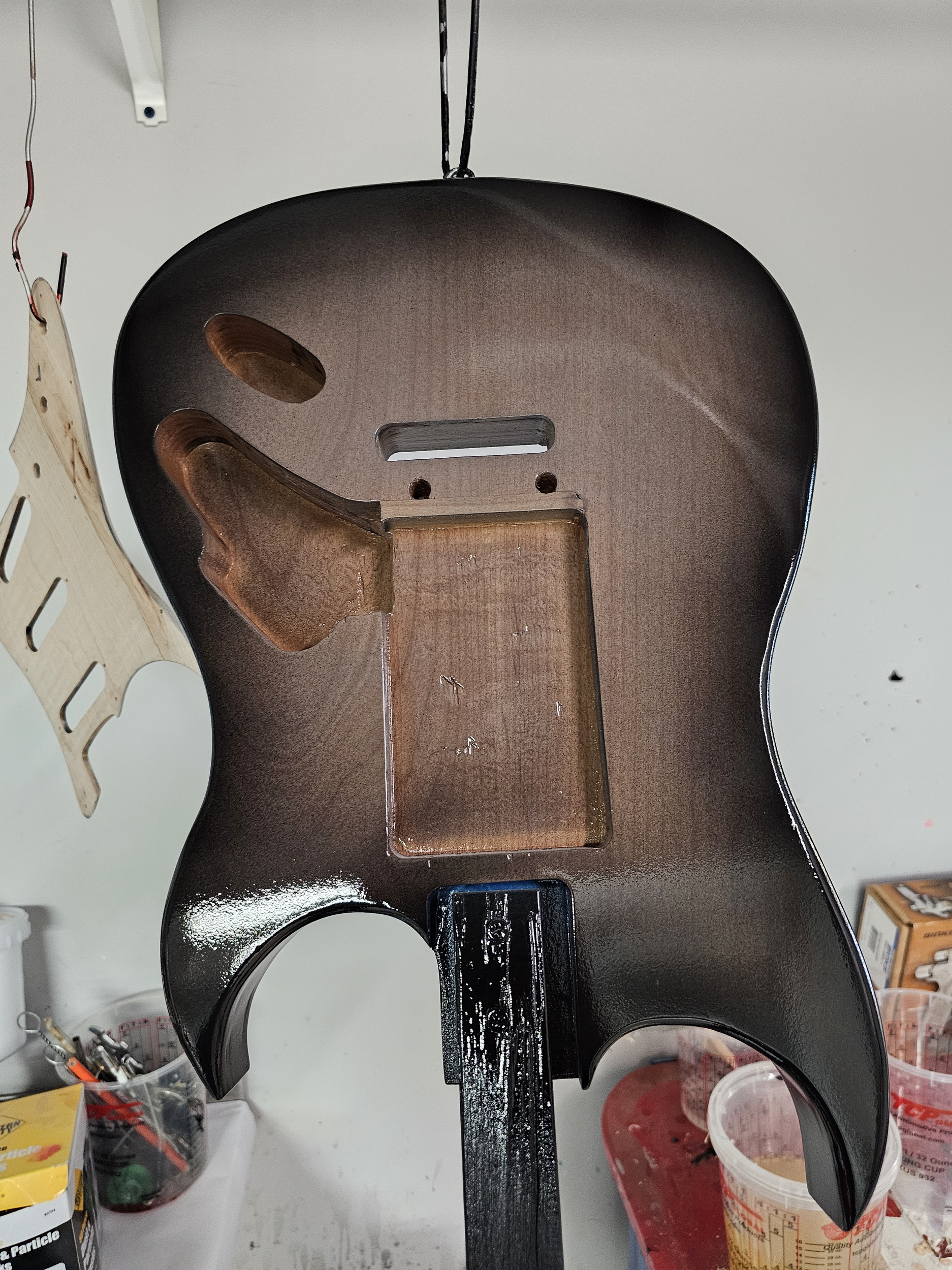Inside of an electric guitar body, showing the hollowed cavity for electronics, with one control cavity and a strap button, painted in a dark glossy finish.