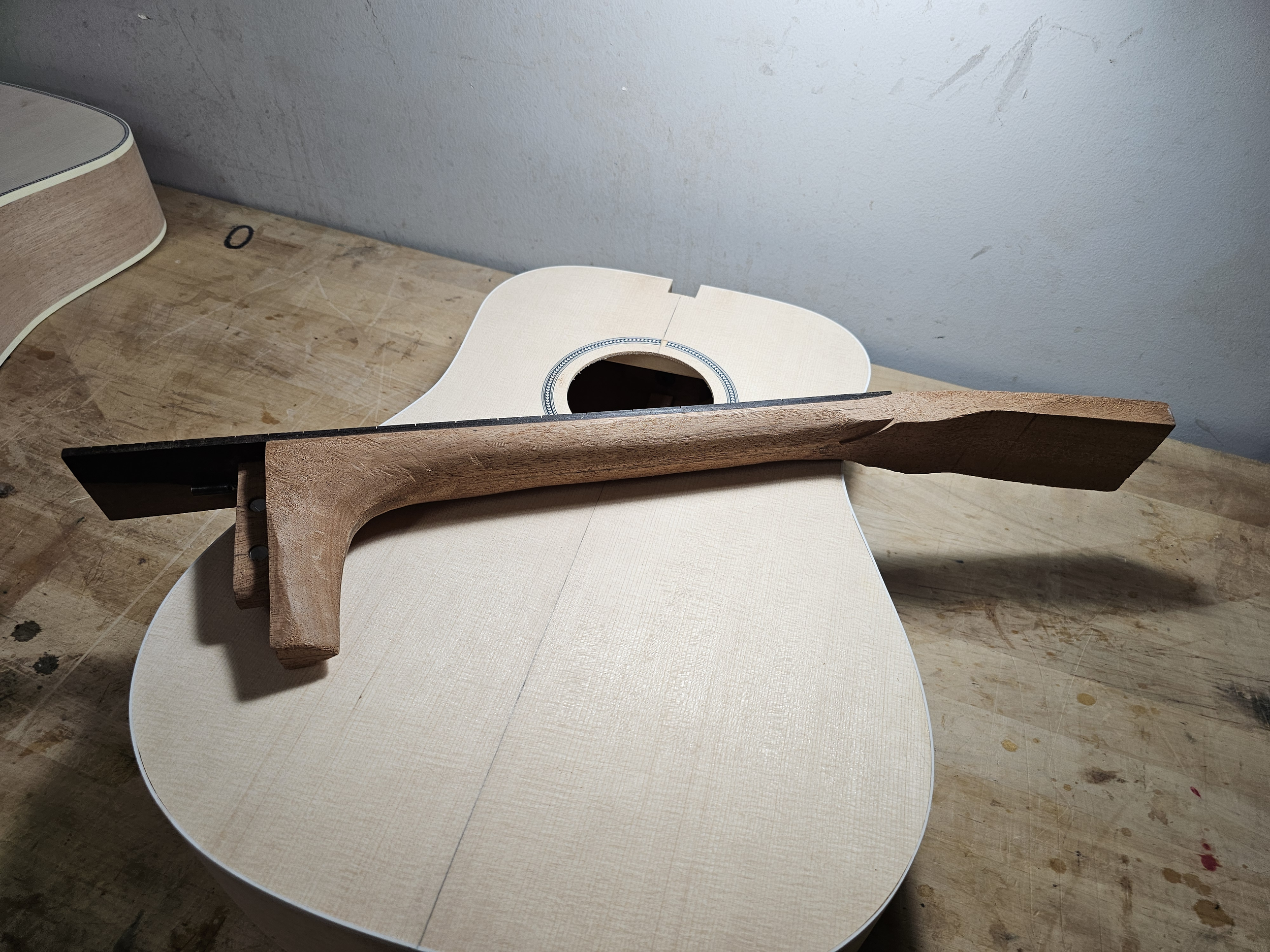 A wooden bridge clamp is placed over an unfinished acoustic guitar body on a workbench.