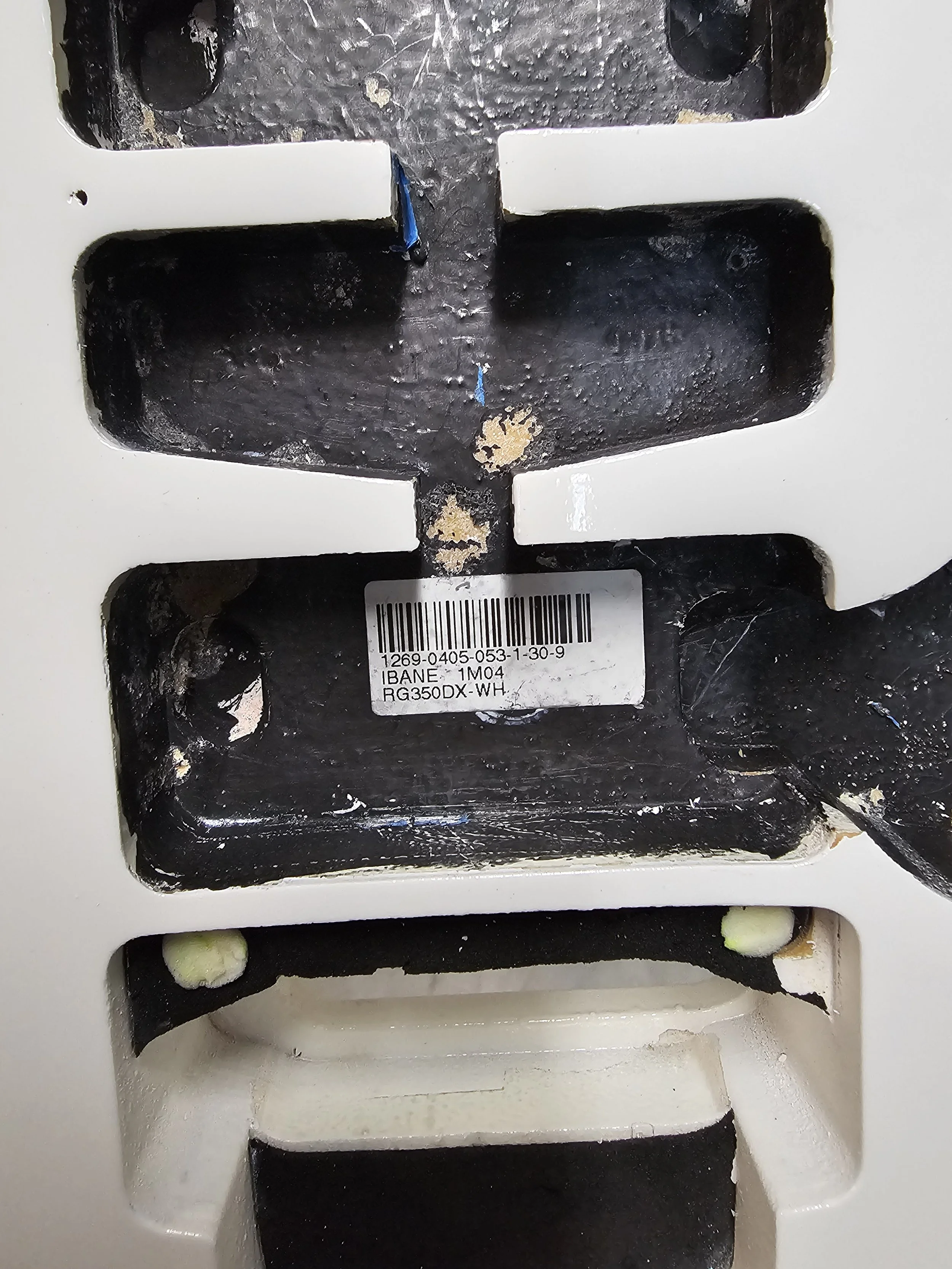 Close-up of a black and white mechanical or electronic device with a barcode label, showing some dirt and chipping paint.