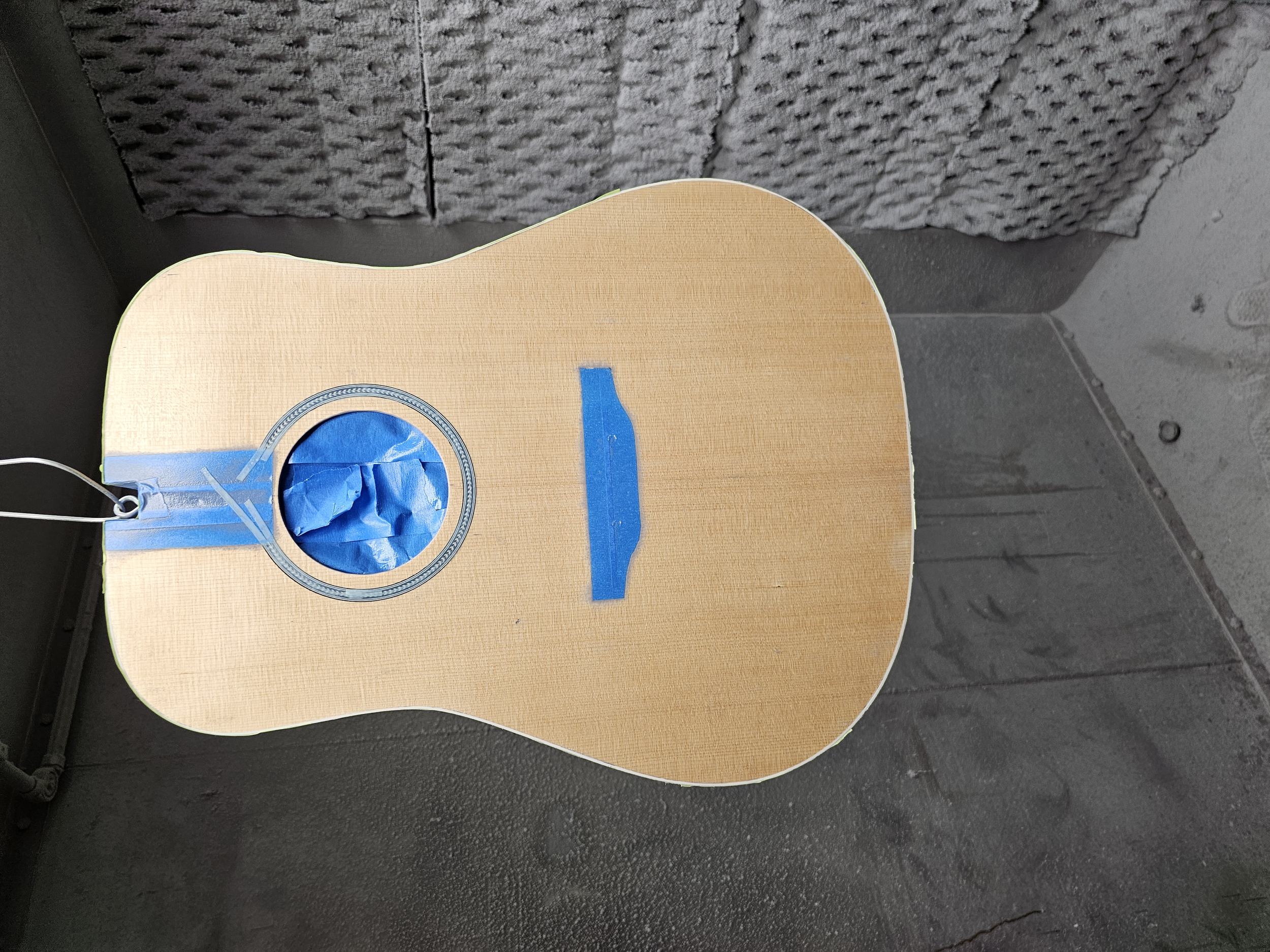 Partially painted acoustic guitar body with masking tape and masking paper in the sound hole.