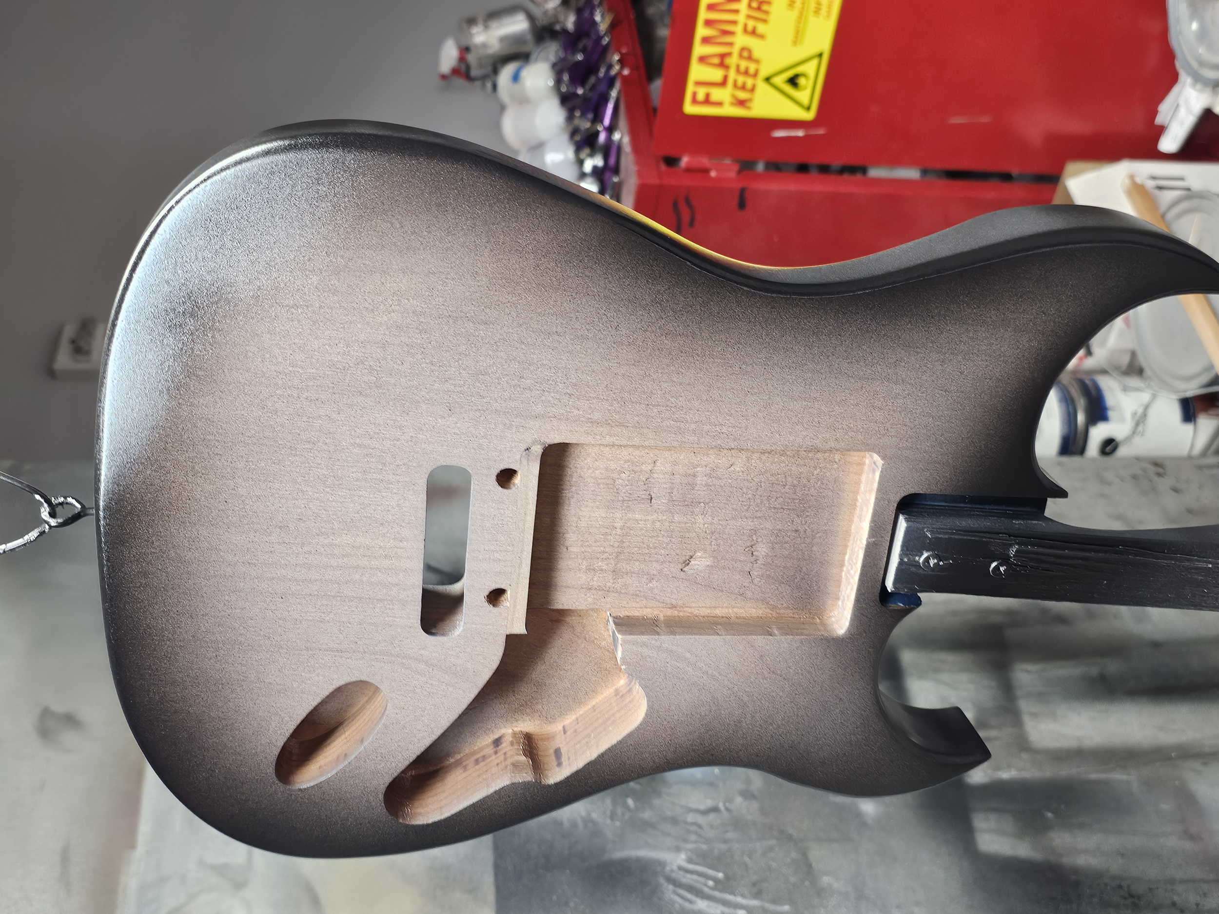Partially assembled electric guitar body with a wood neck, in a workshop setting.