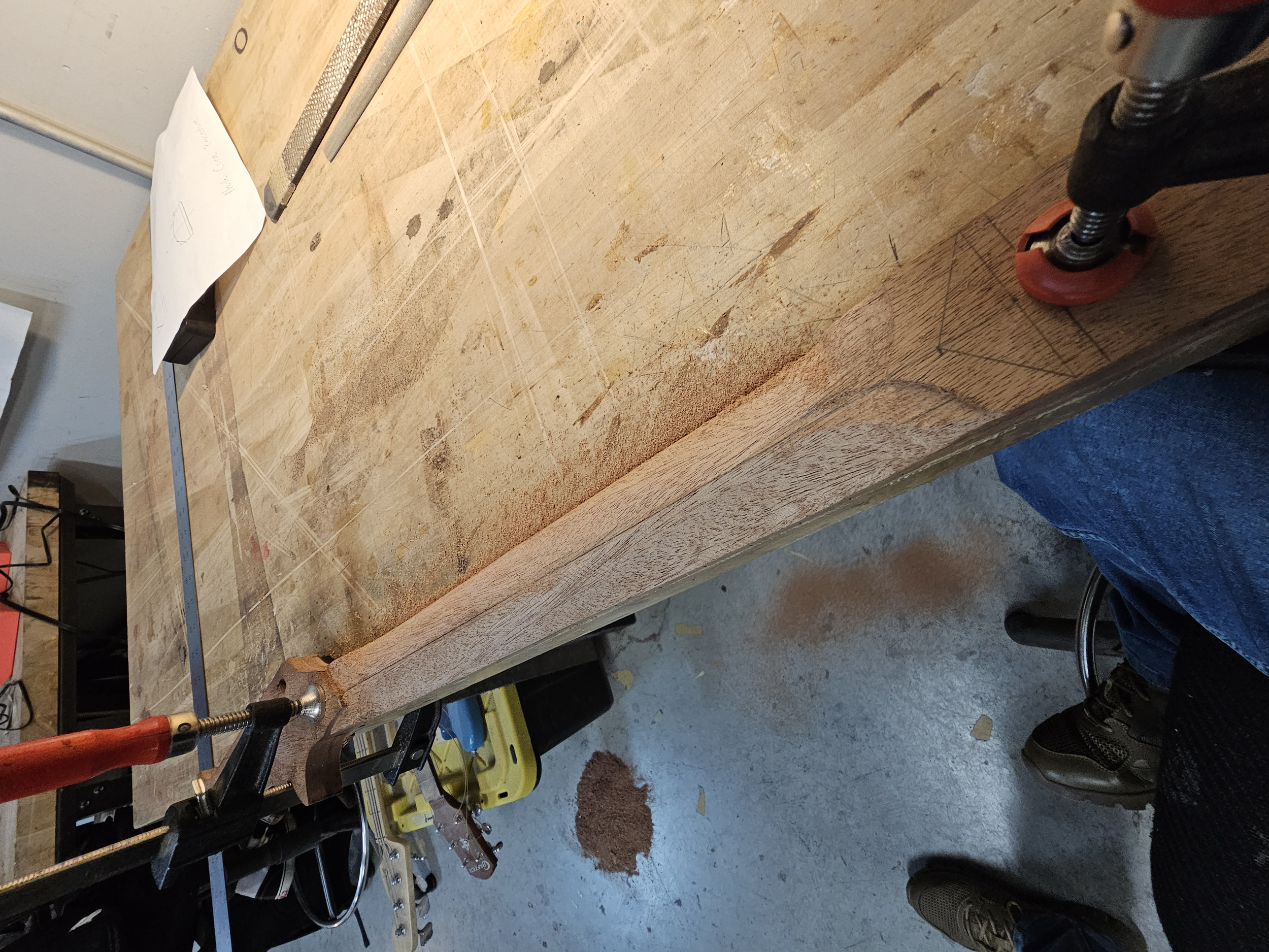 Woodworking workbench with a piece of wood being marked with measurements and angles, clamps securing the wood, and various tools around.