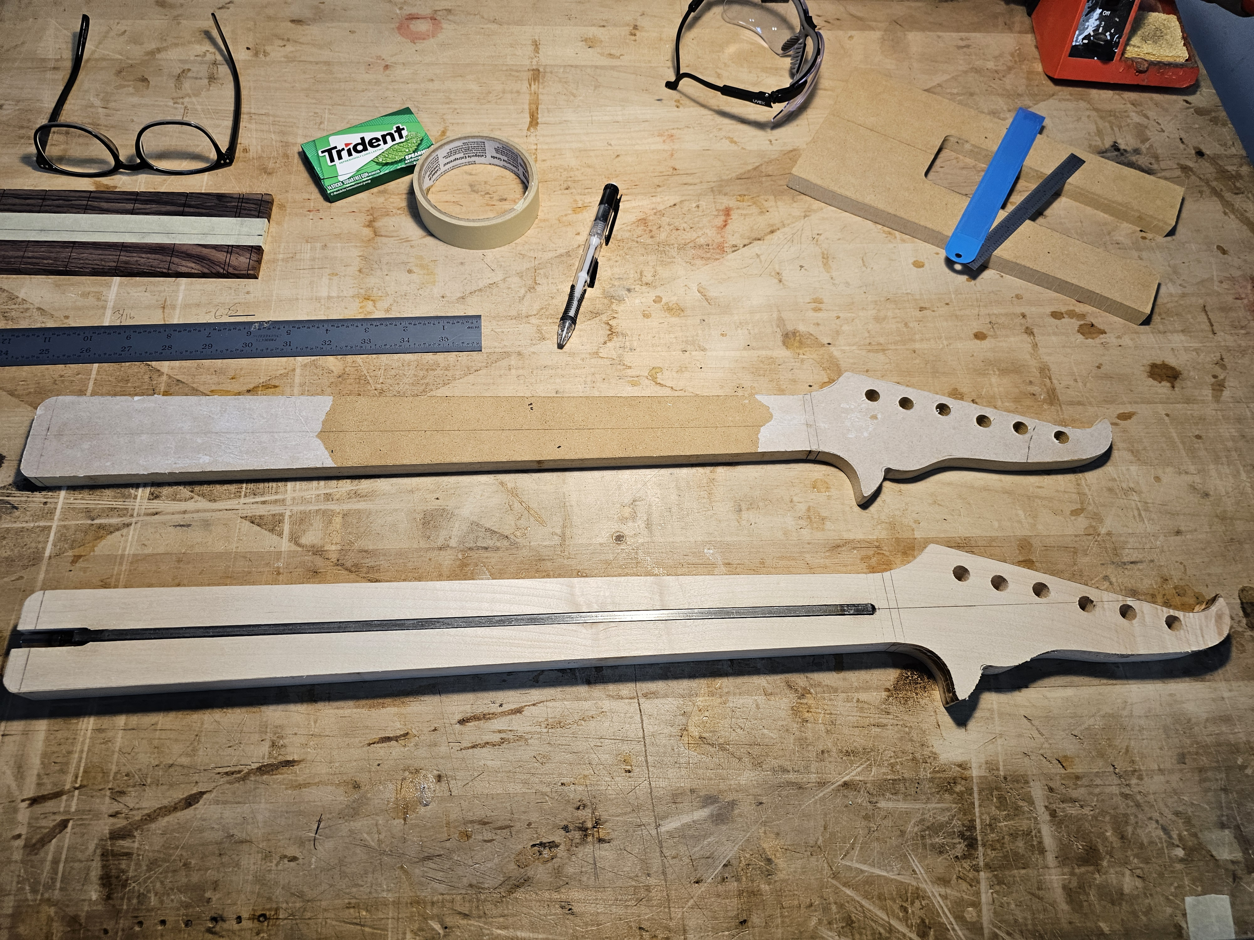 Workbench with guitar neck templates, measuring tools, tape, pens, and other woodworking accessories.