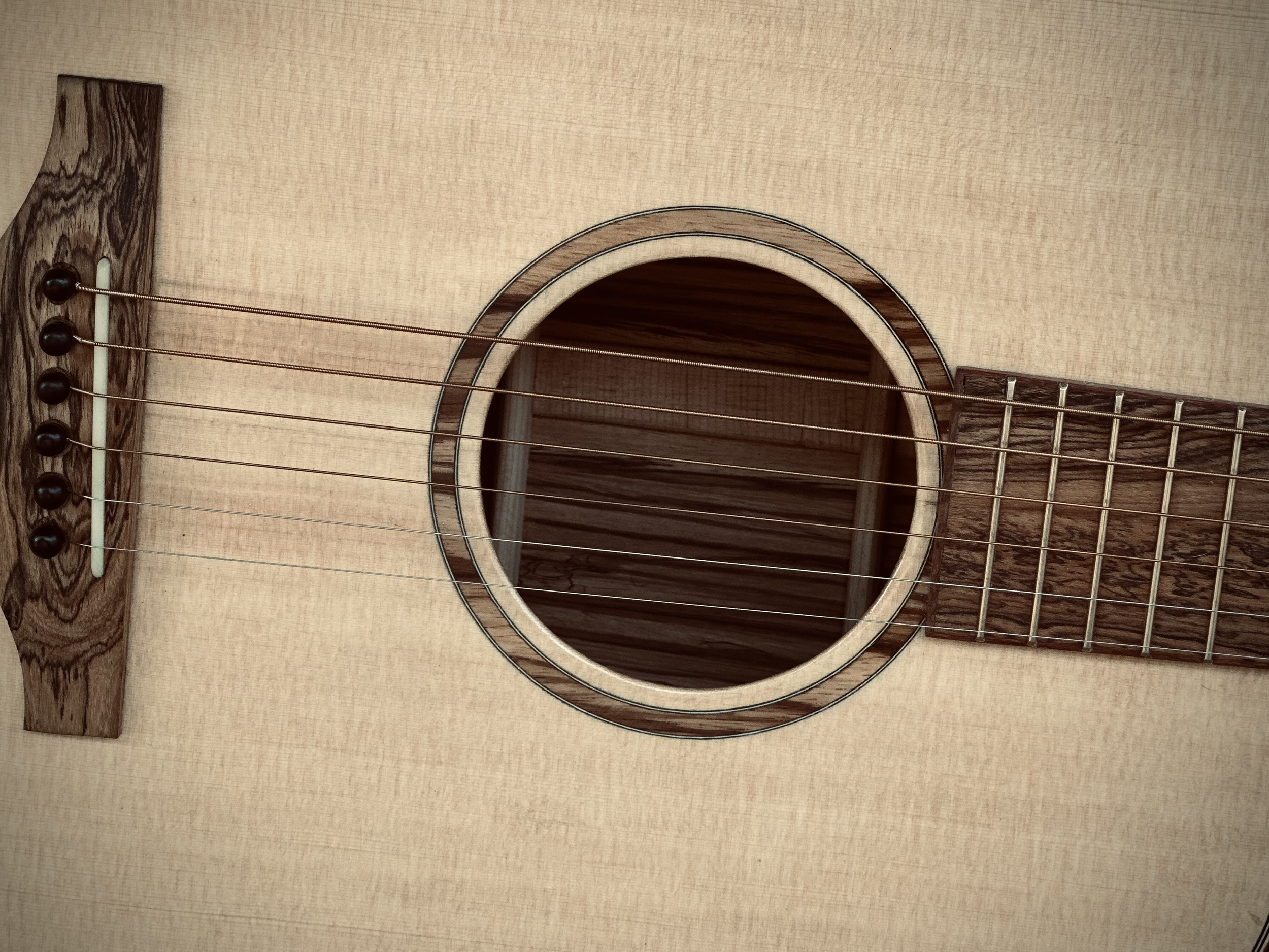 Close-up of an acoustic guitar's sound hole, strings, and body, made of light-colored wood with dark wood accents.