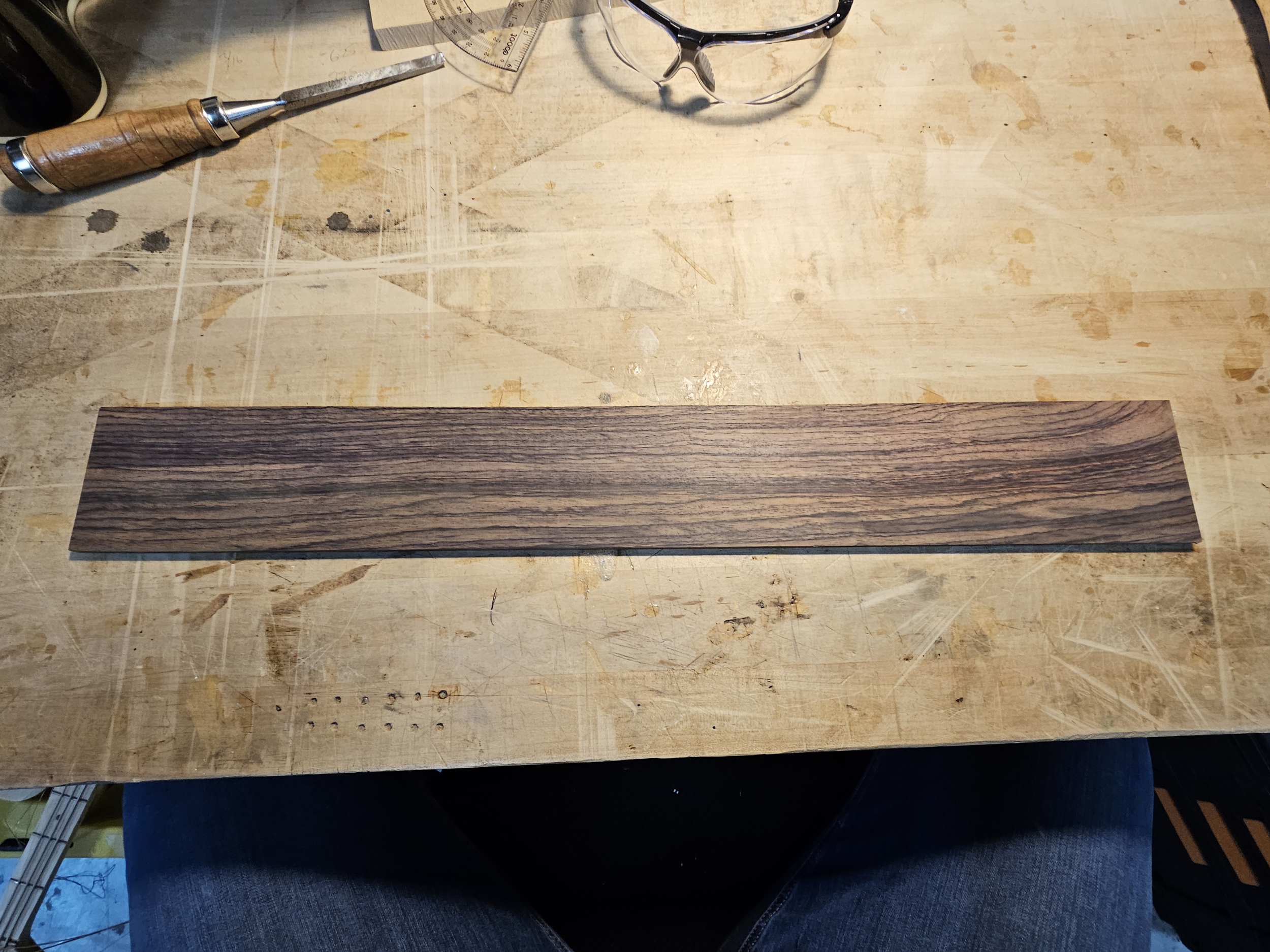 A strip of wood with dark and light brown grain pattern on a workbench.