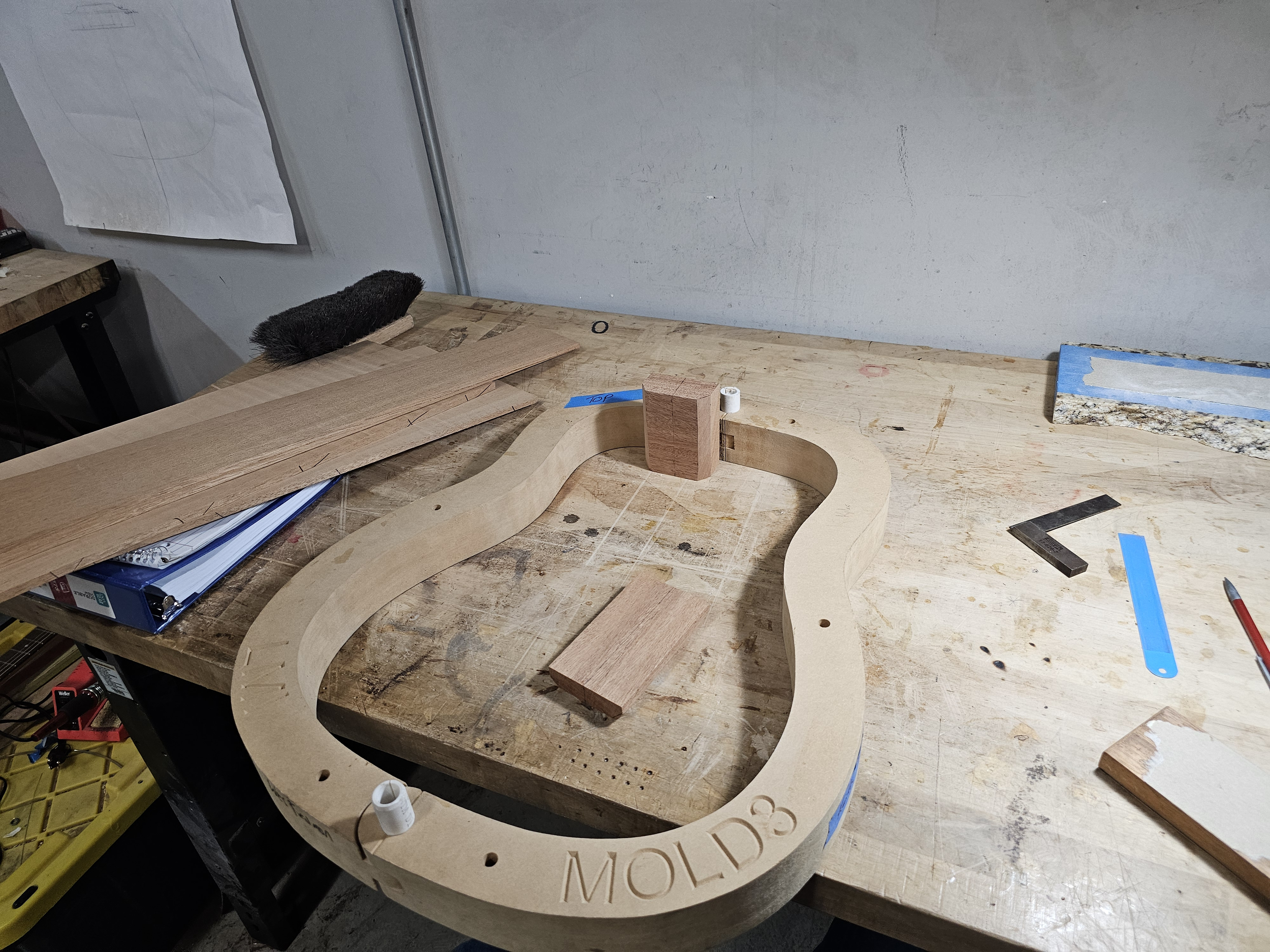 Woodworking workshop with a wooden frame that has the word 'MOULD' engraved on it, placed on a workbench with various tools and pieces of wood.