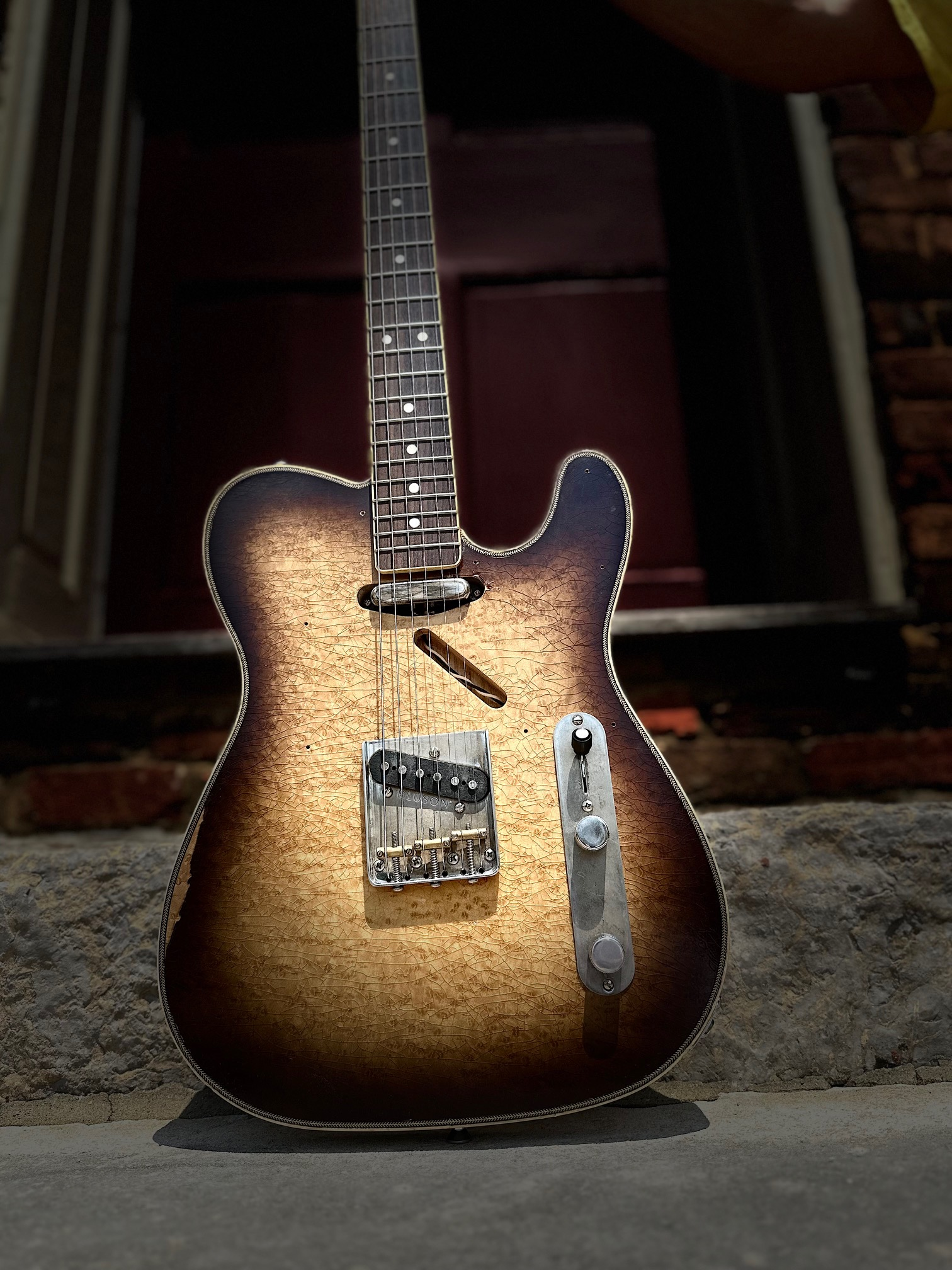 Vintage electric guitar with a cracked sunburst finish resting against stone surface with brick wall background.