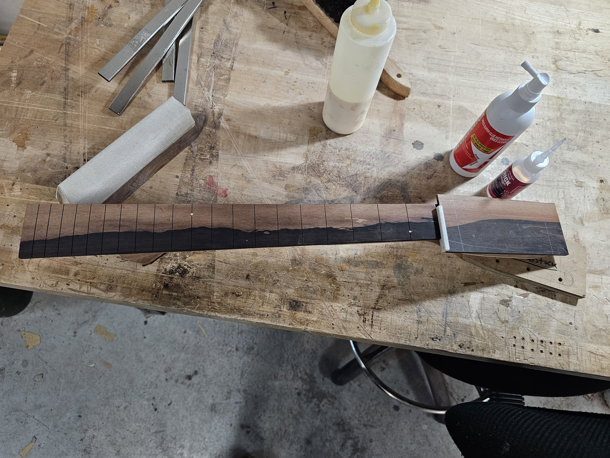 A woodworking workspace with a partially assembled ukulele neck, woodworking tools, glue, and fillers on a workbench.