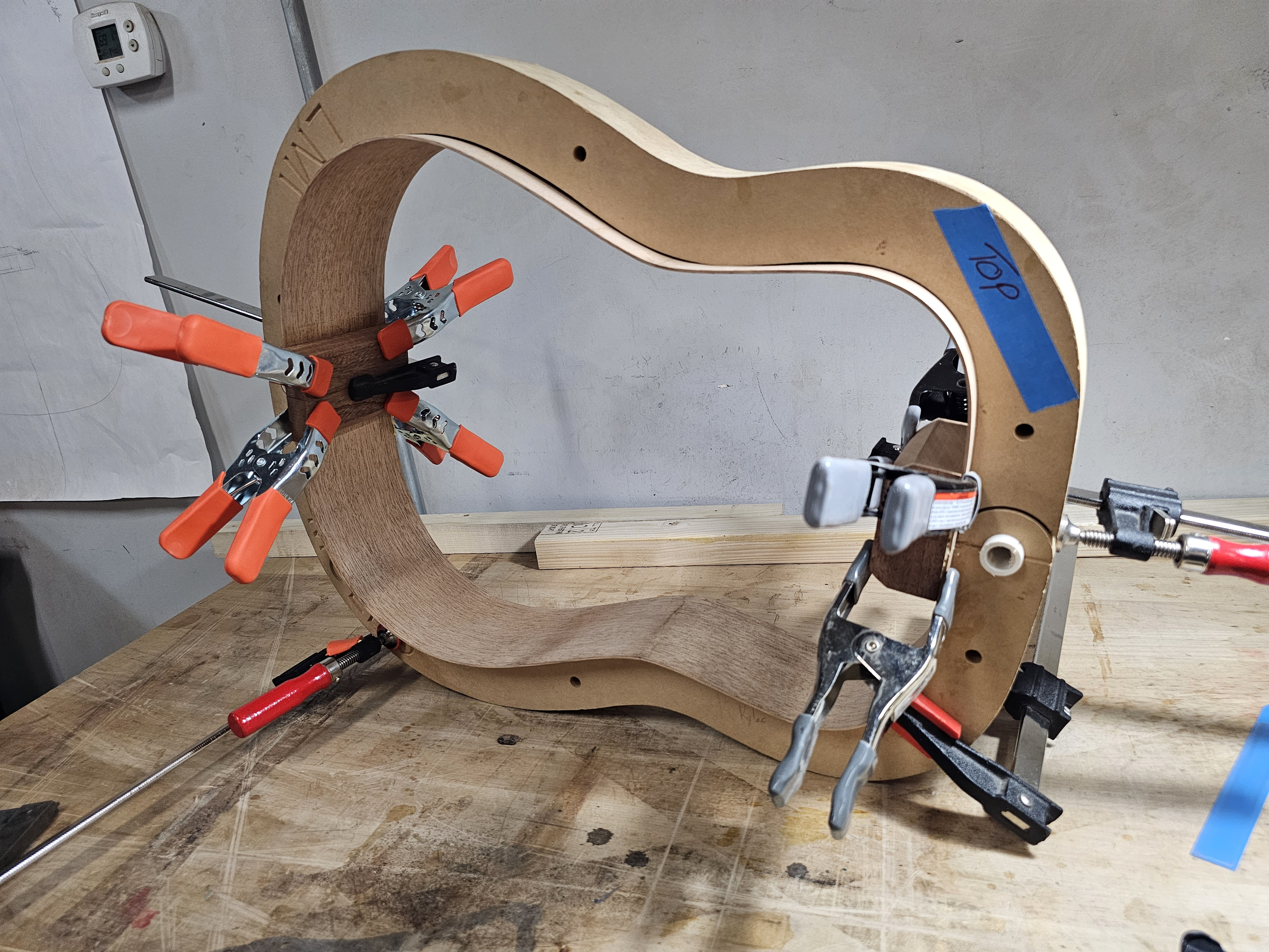 Woodwork in progress with a curved wooden frame secured by several clamps on a workbench.