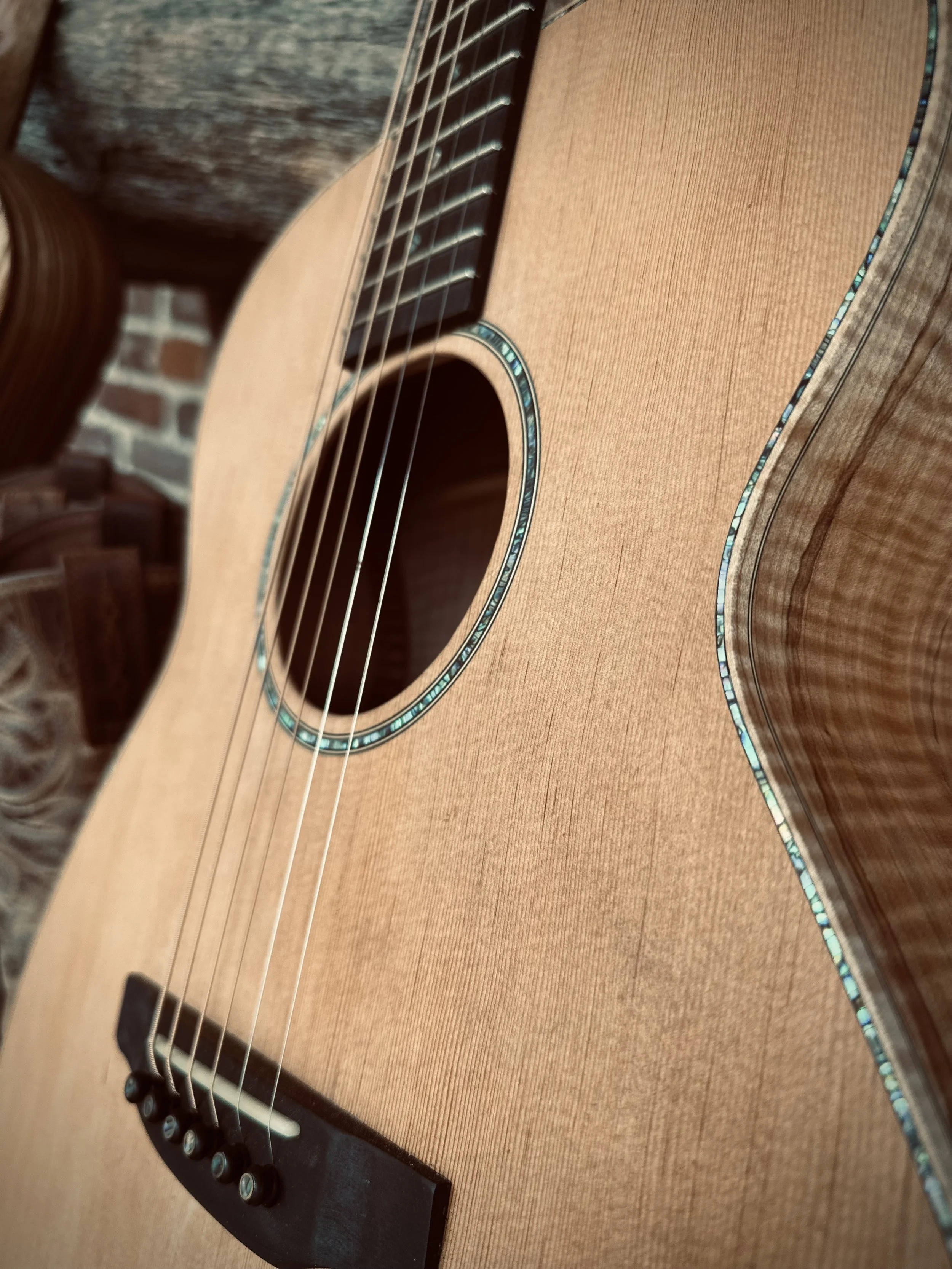 Close-up of an acoustic guitar with a natural wood finish, decorative inlay around the sound hole, and a brick wall in the background.