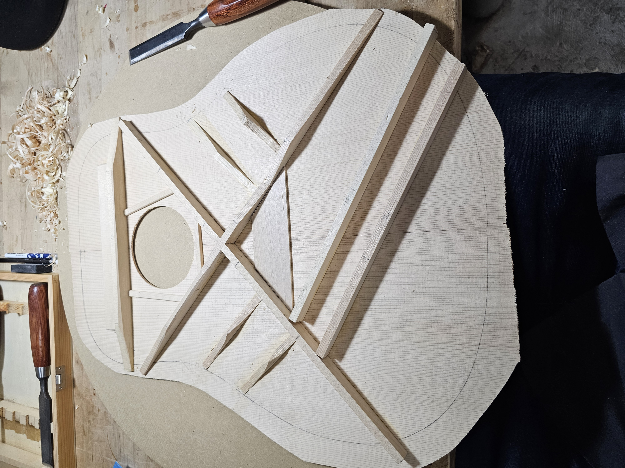 Wooden guitar body with braces and circular cutout in progress on a workbench.