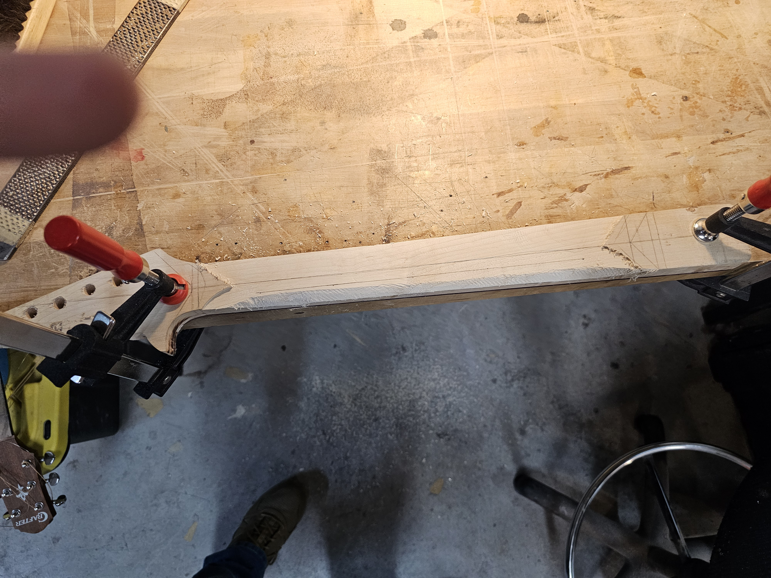 Clamped piece of wood on a workbench with marked lines and a curved cut section.
