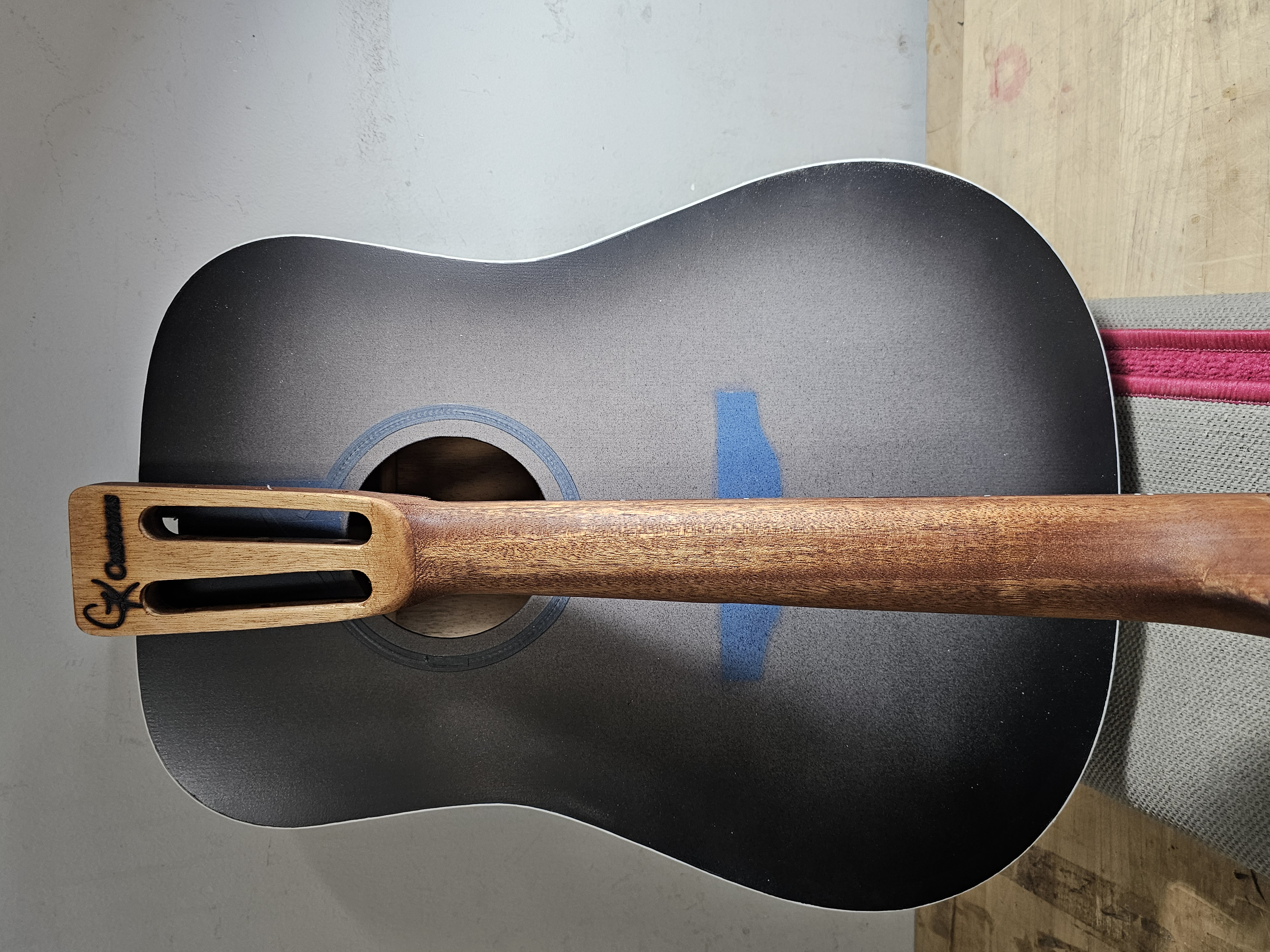 Close-up of an acoustic guitar lying on a dark guitar case, with a wooden spatula resting on the guitar's sound hole.
