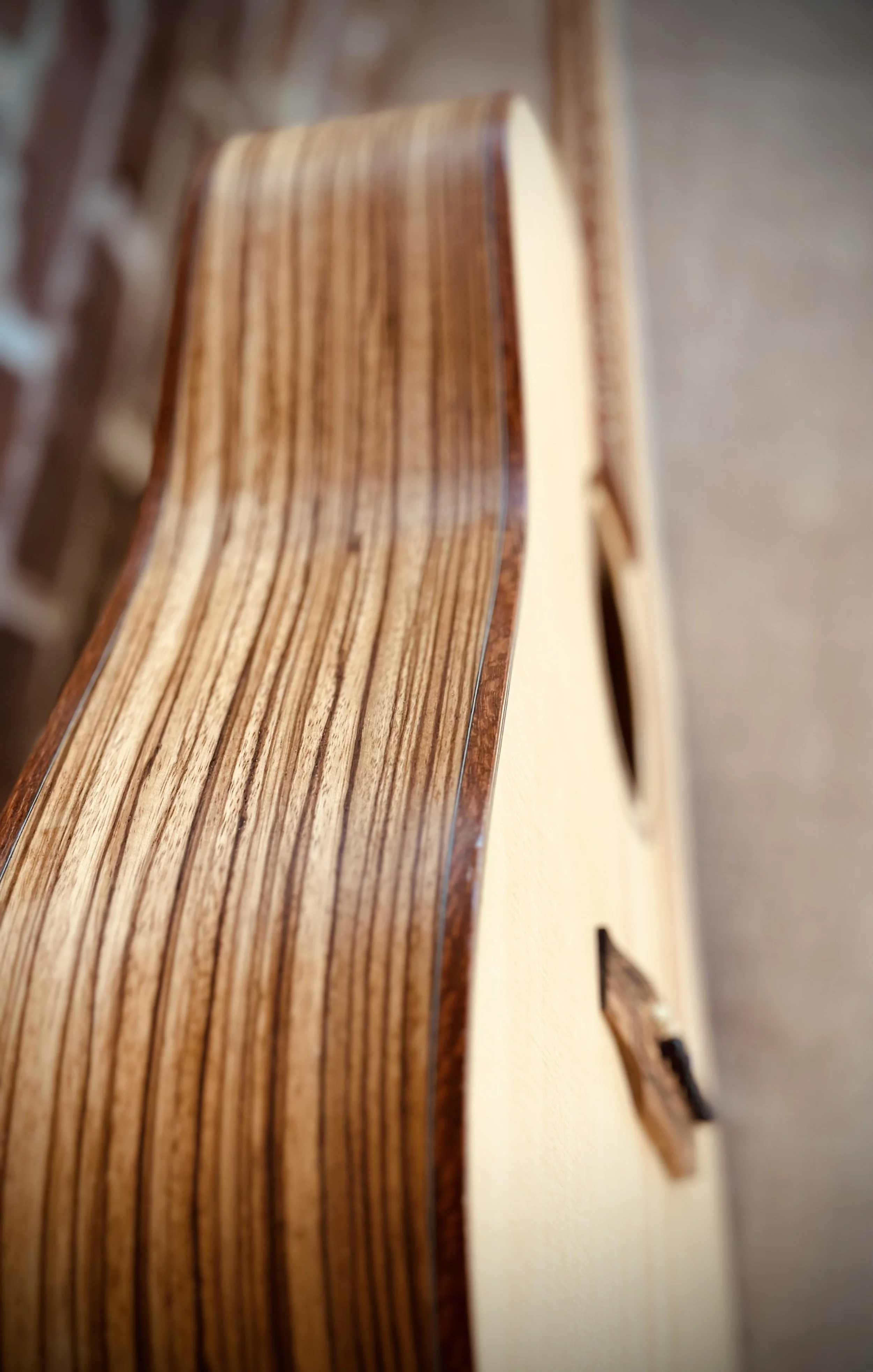 Close-up of the edge of an acoustic guitar, showing the wooden top with a glossy finish and a darker wooden binding.