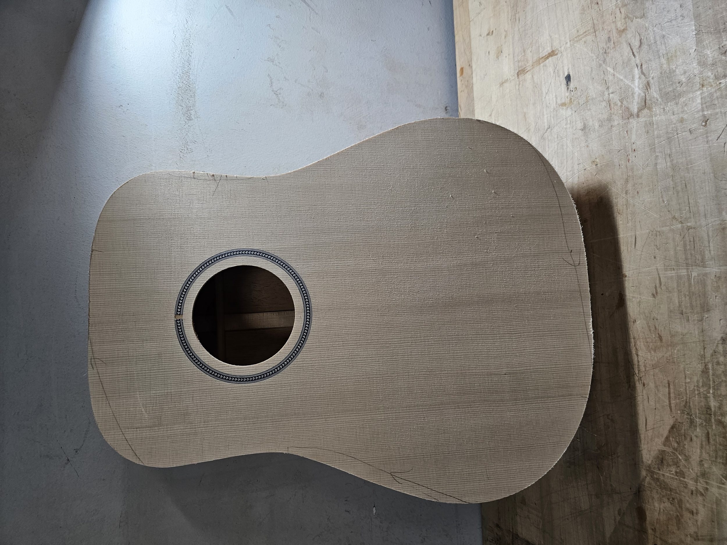 Unfinished wooden guitar body with a sound hole, placed on a workbench in a workshop.