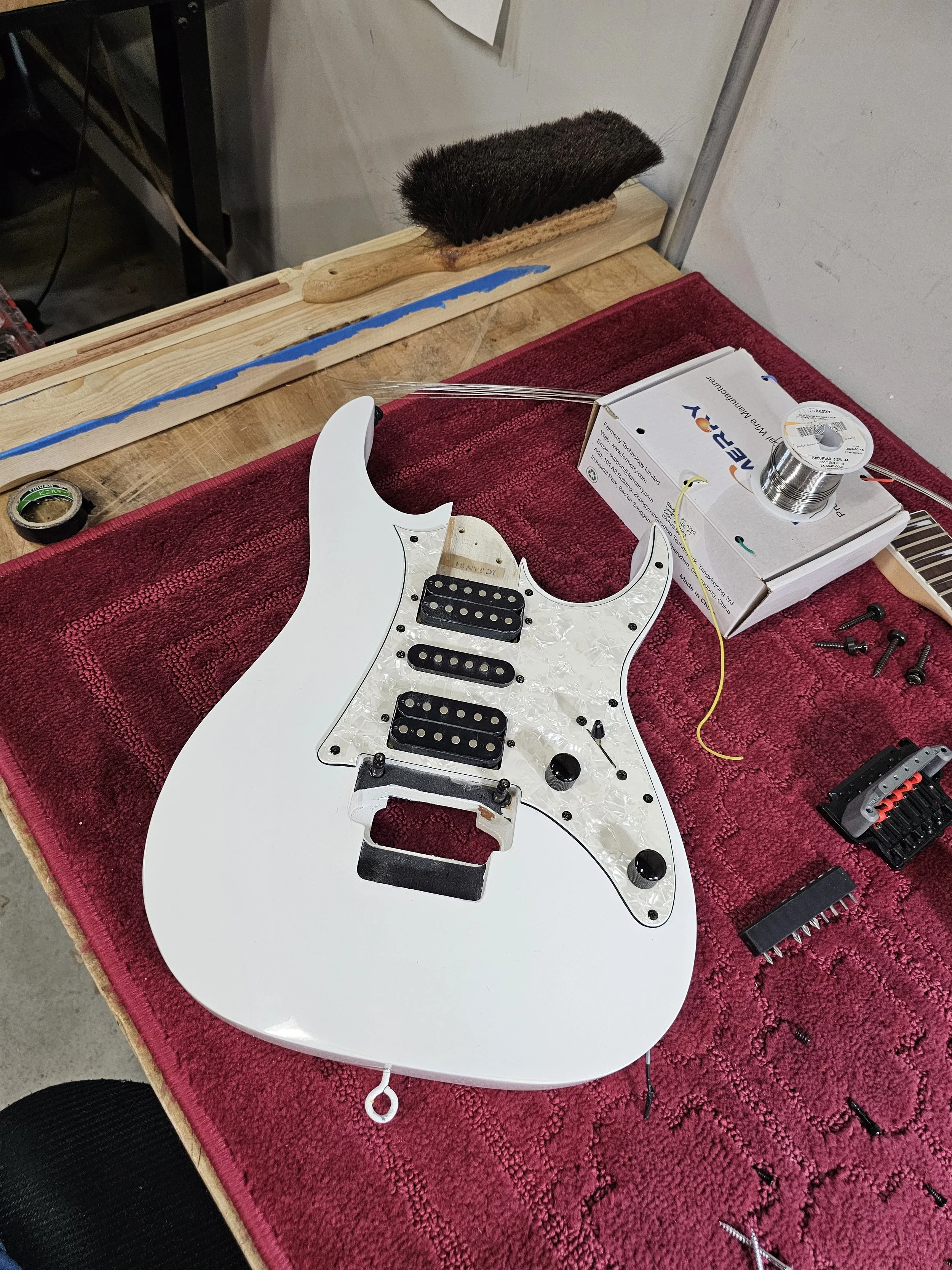 Disassembled electric guitar body with pickups, on a red towel, with tools and parts around it.