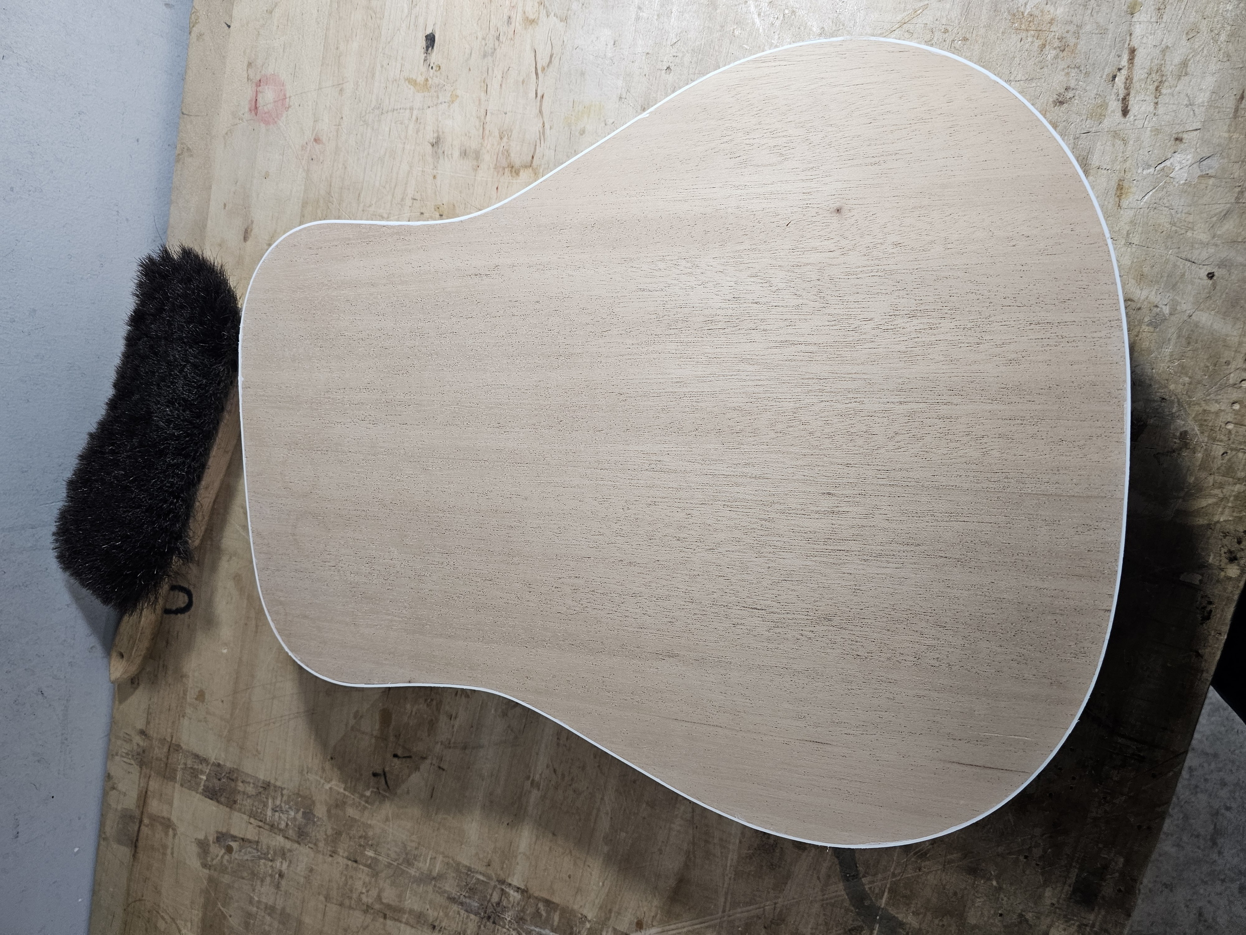 Unfinished wooden guitar body with white outline on a workbench.