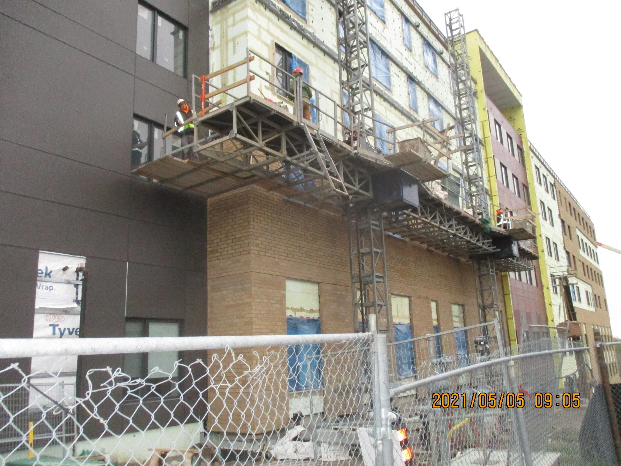Construction workers wearing safety gear working on scaffolding outside a building during daylight.
