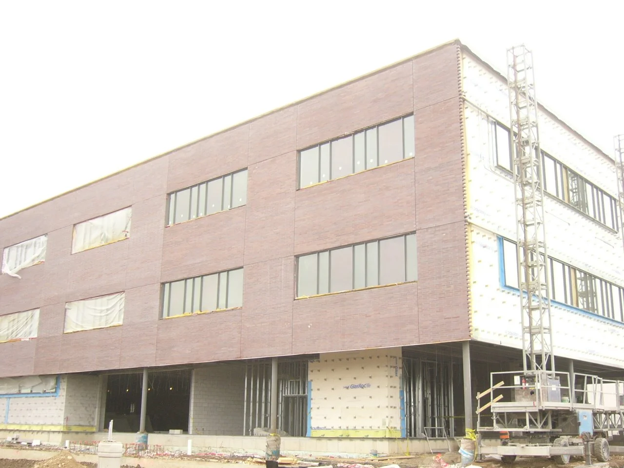 Under construction building with four floors and large windows, scaffolding on the right side, and construction materials on the ground.