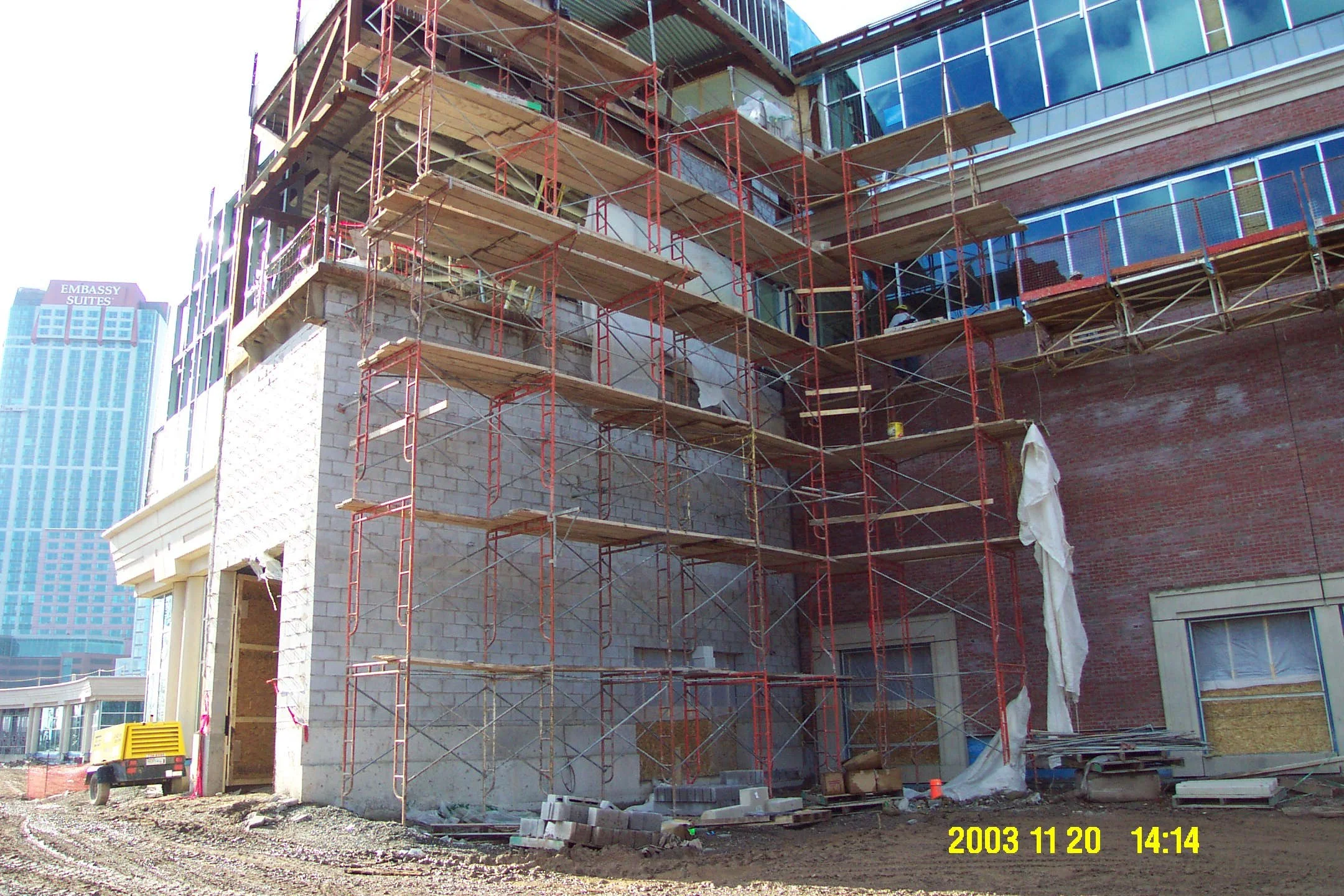 Construction site with scaffolding; building walls in progress; city buildings visible in background; date and time stamp: November 20, 2003, 2:14 PM.