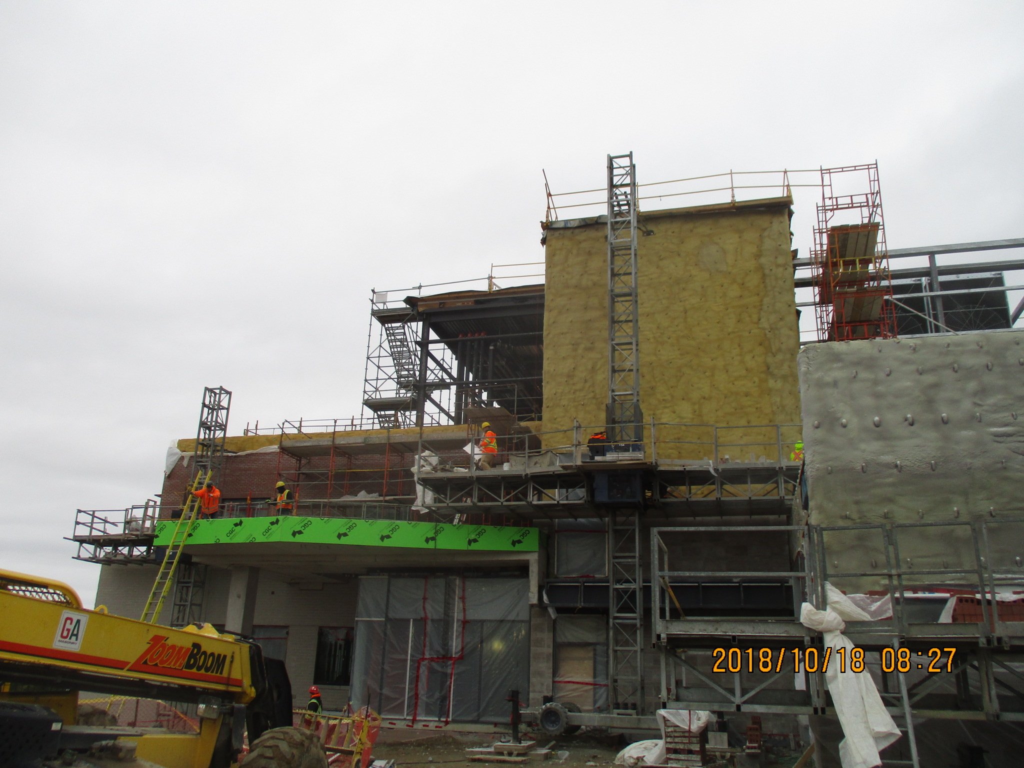 Construction workers and scaffolding at a building site with overcast sky, showing ongoing structure work and insulation being installed.