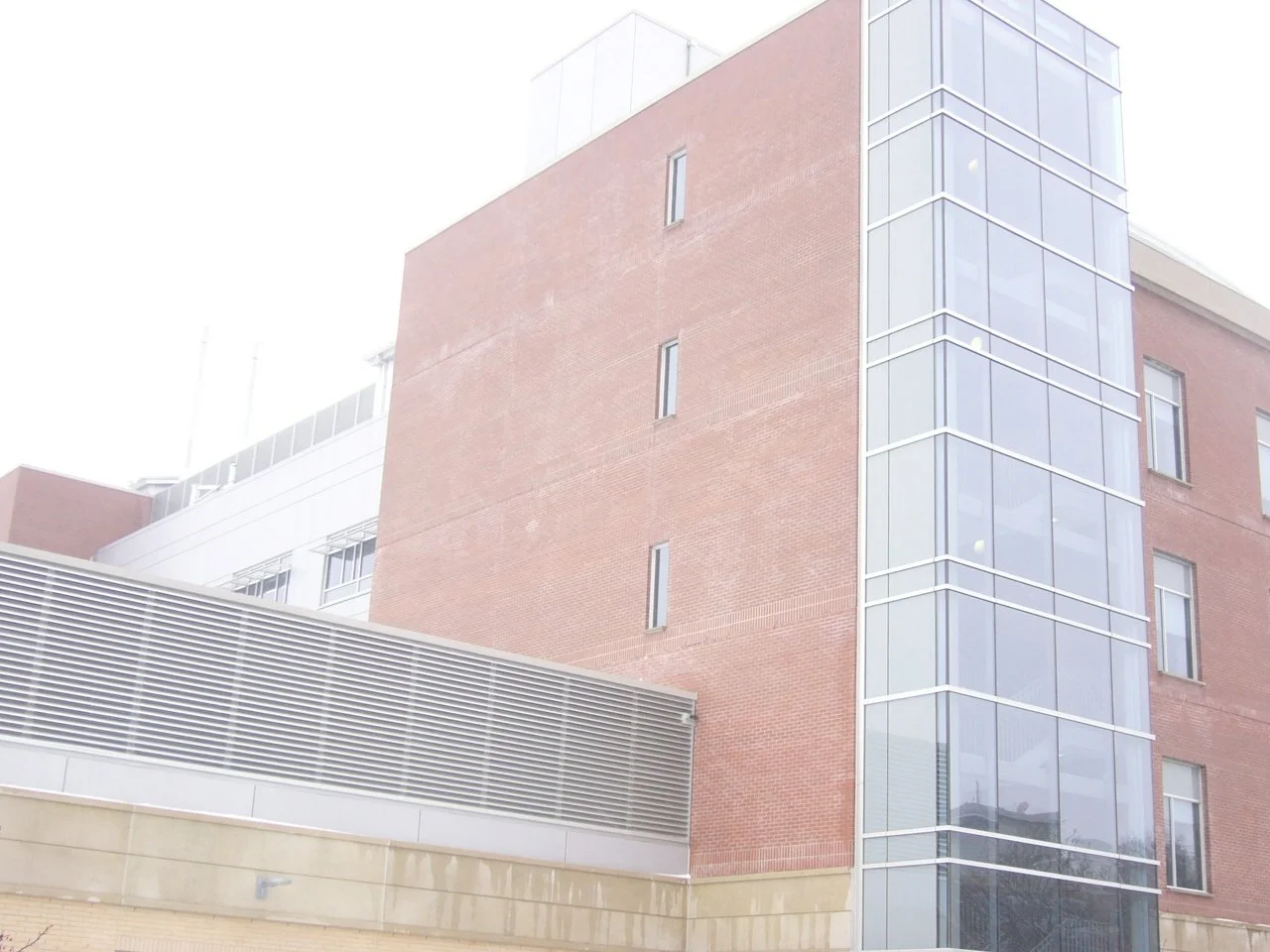 A modern multi-story building with a curved glass corner and a brick facade.
