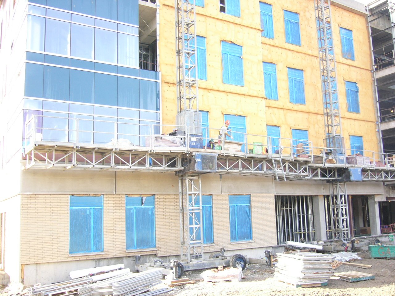 Construction site with a partially built multi-story building, blue window coverings, and construction workers on scaffolding.