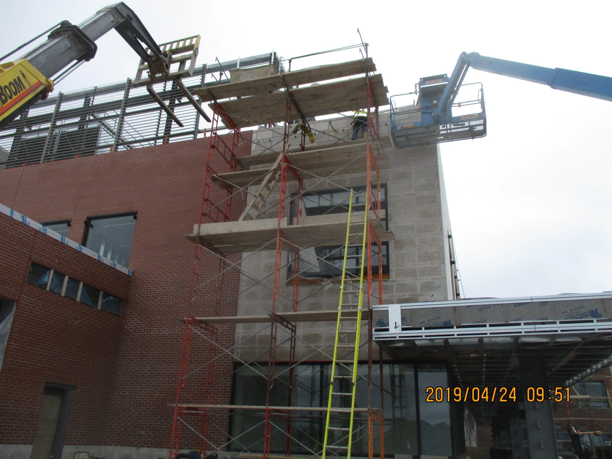 Construction site with scaffolding and cranes on a multi-story building, with a brick facade and large windows, during daytime.
