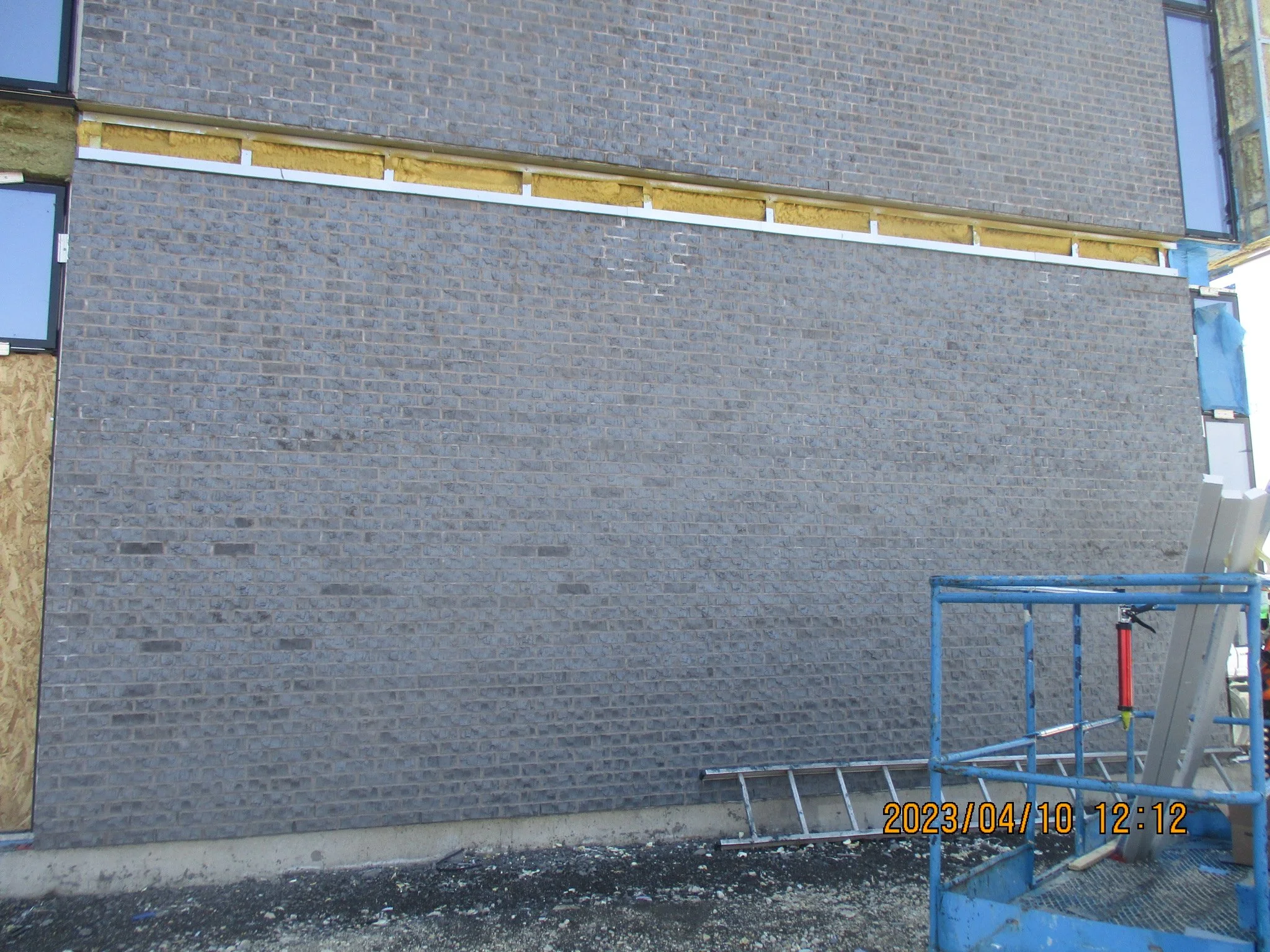 A brick building under construction with a large gray brick wall andConstruction equipment in the foreground.