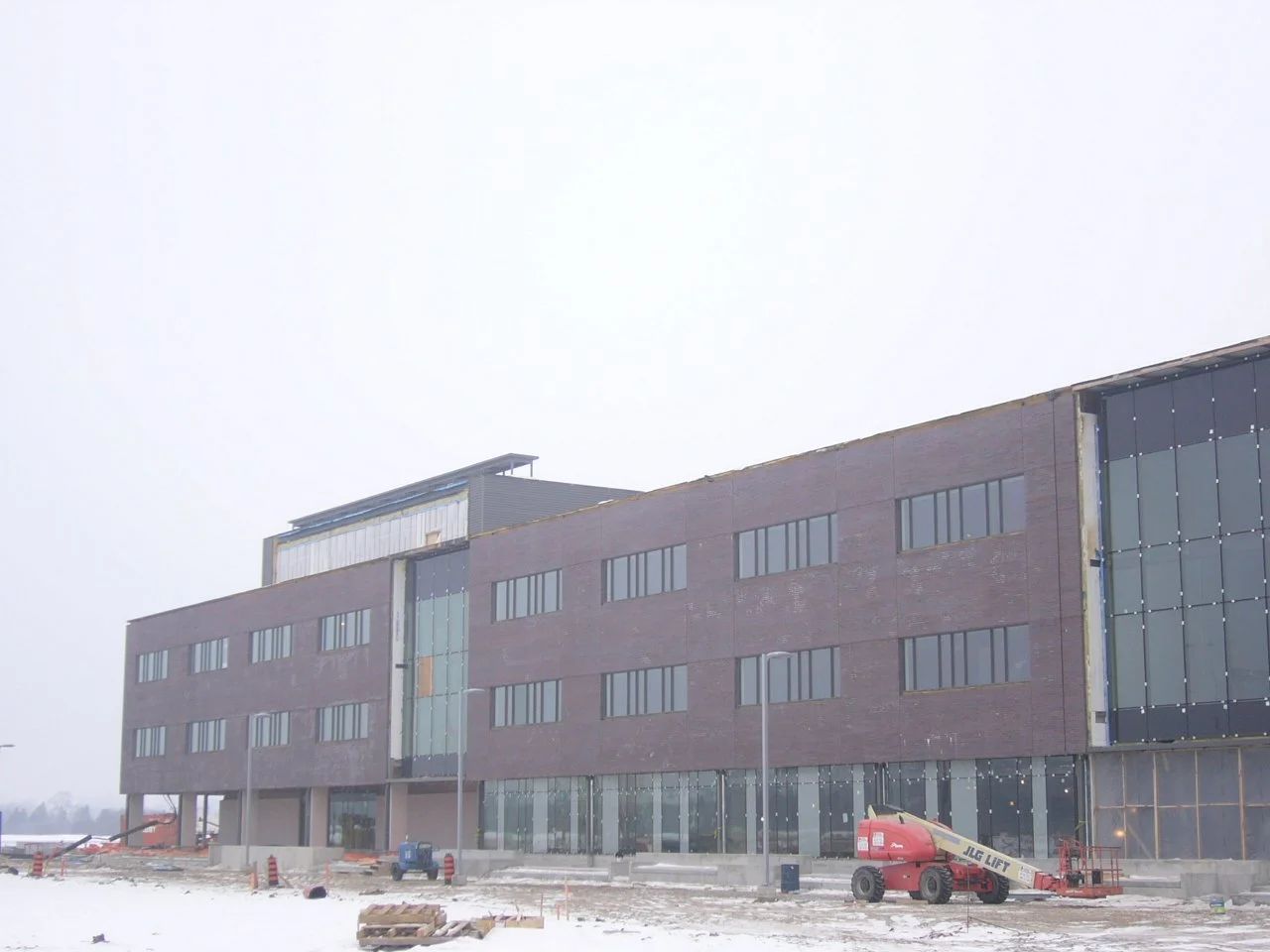 Under construction multi-story building with large windows and scaffolding, construction equipment, and snow on the ground.