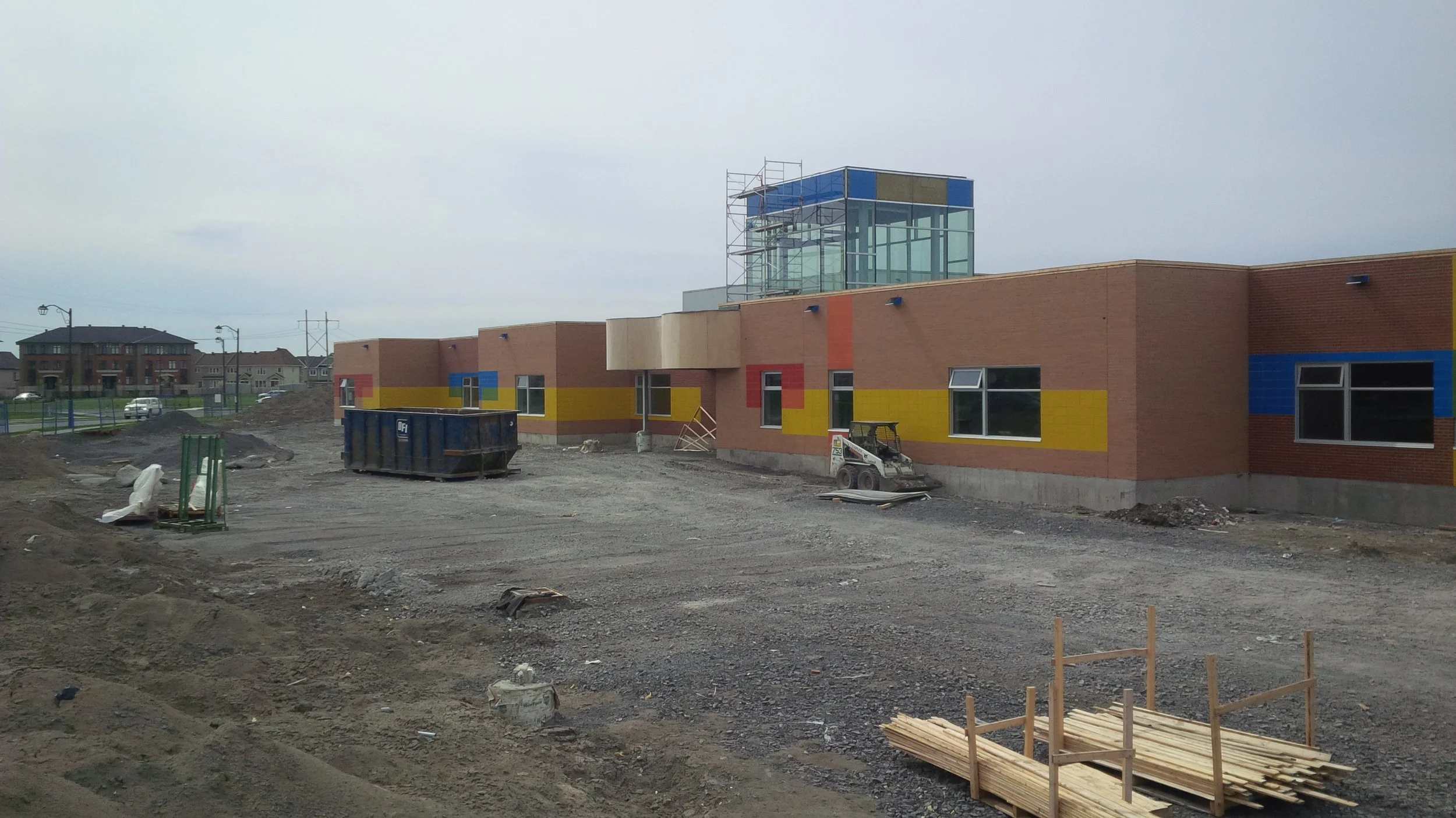 Building under construction with colorful exterior walls, construction equipment, and materials on a dirt lot.