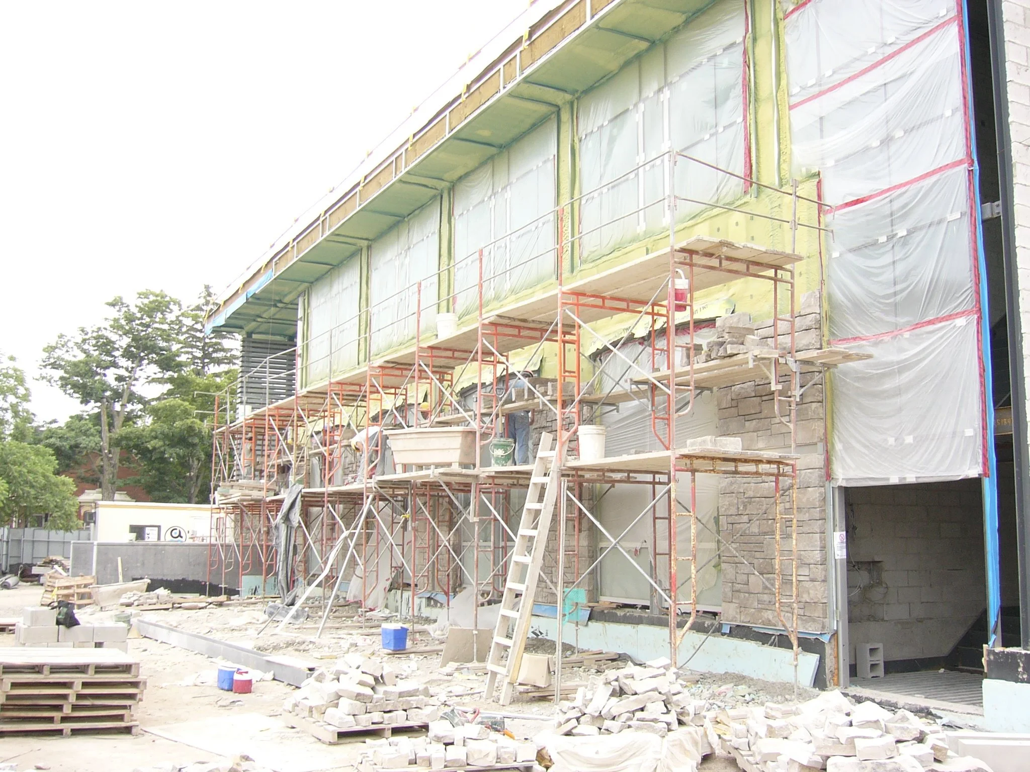Construction site with scaffolding and workers building a multi-story building, with brickwork and construction materials scattered around.