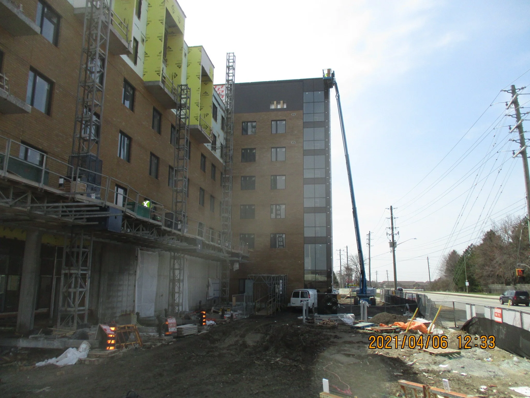 Construction site with building under construction, scaffolding, a crane, a white truck, and electrical poles on the right, with a cloudy sky in the background.