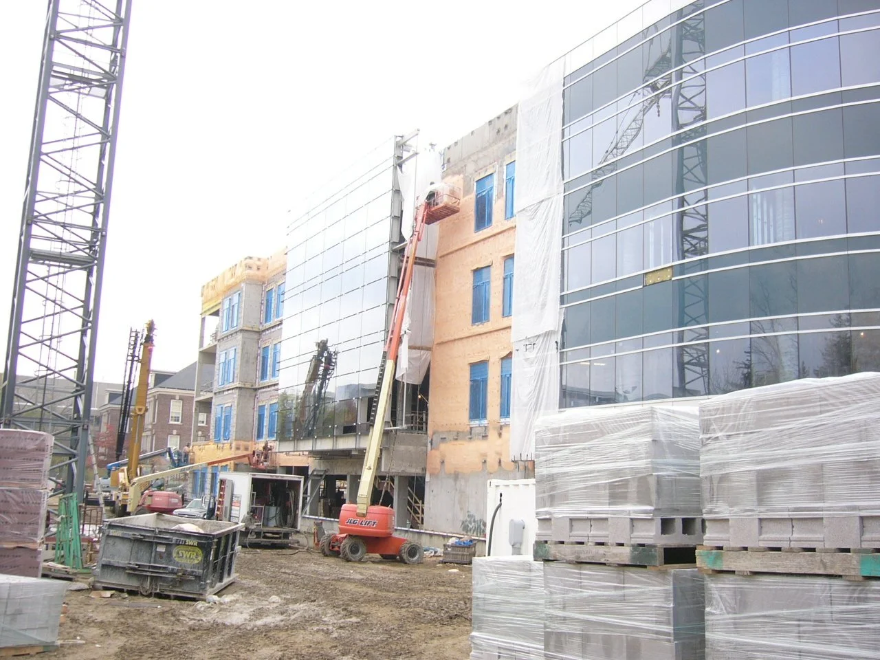 Construction site with building under construction, including scaffolding, construction cranes, and building materials wrapped in plastic.