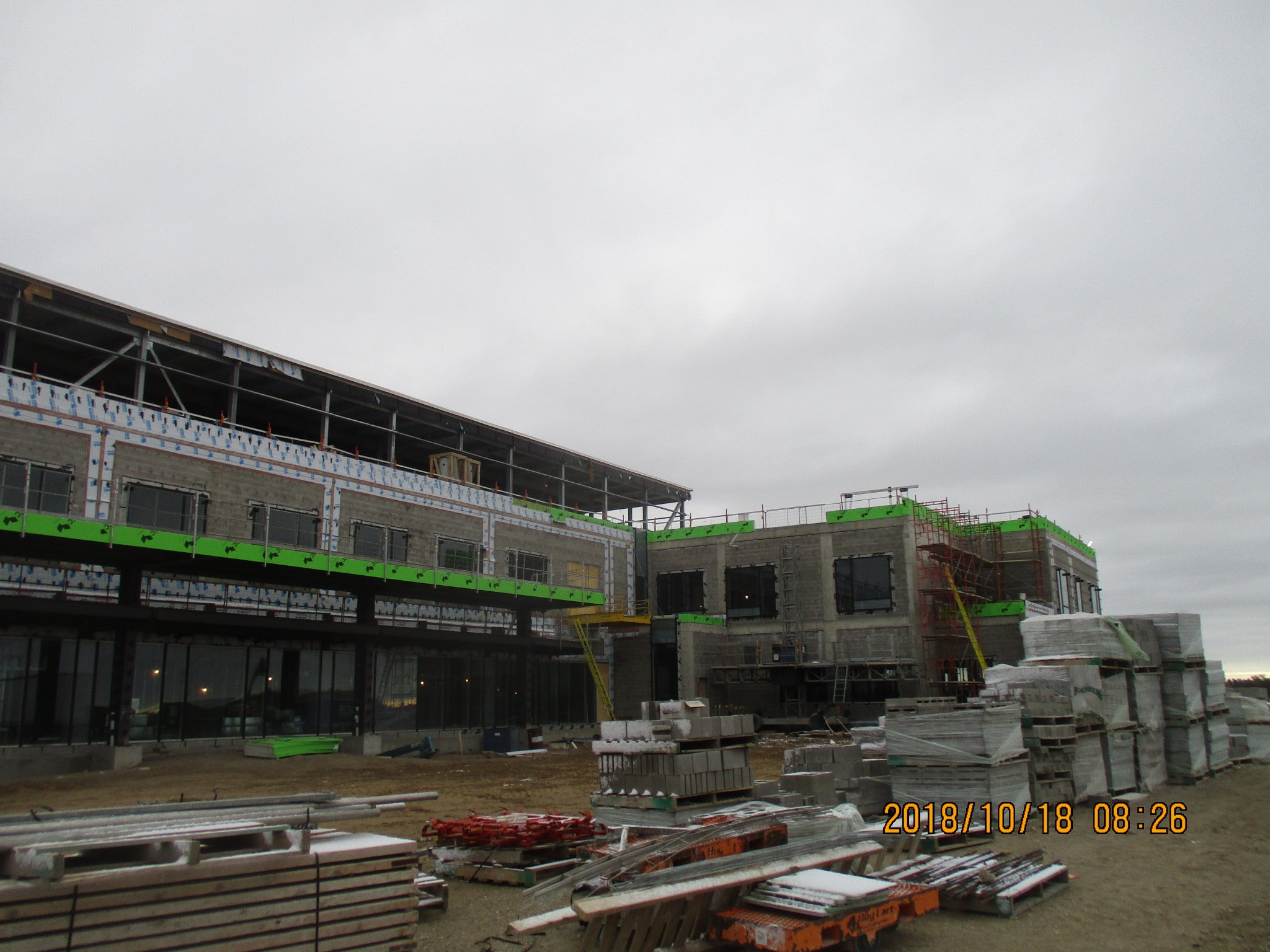 Construction site with a multi-story building under construction, scaffolding, construction materials, and overcast sky.