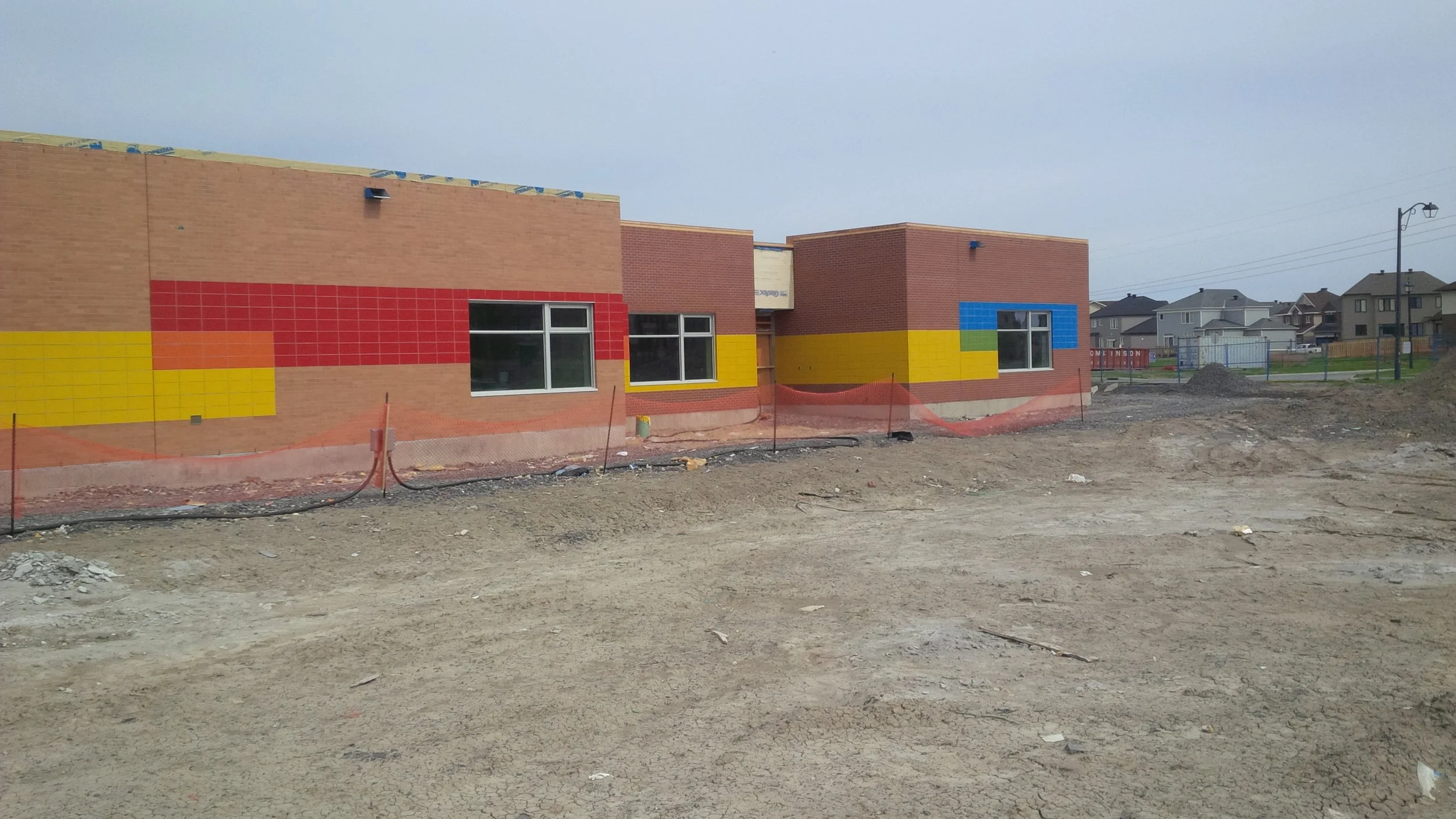 Under construction building with colorful brick and tile exterior, and surrounding dirt ground.
