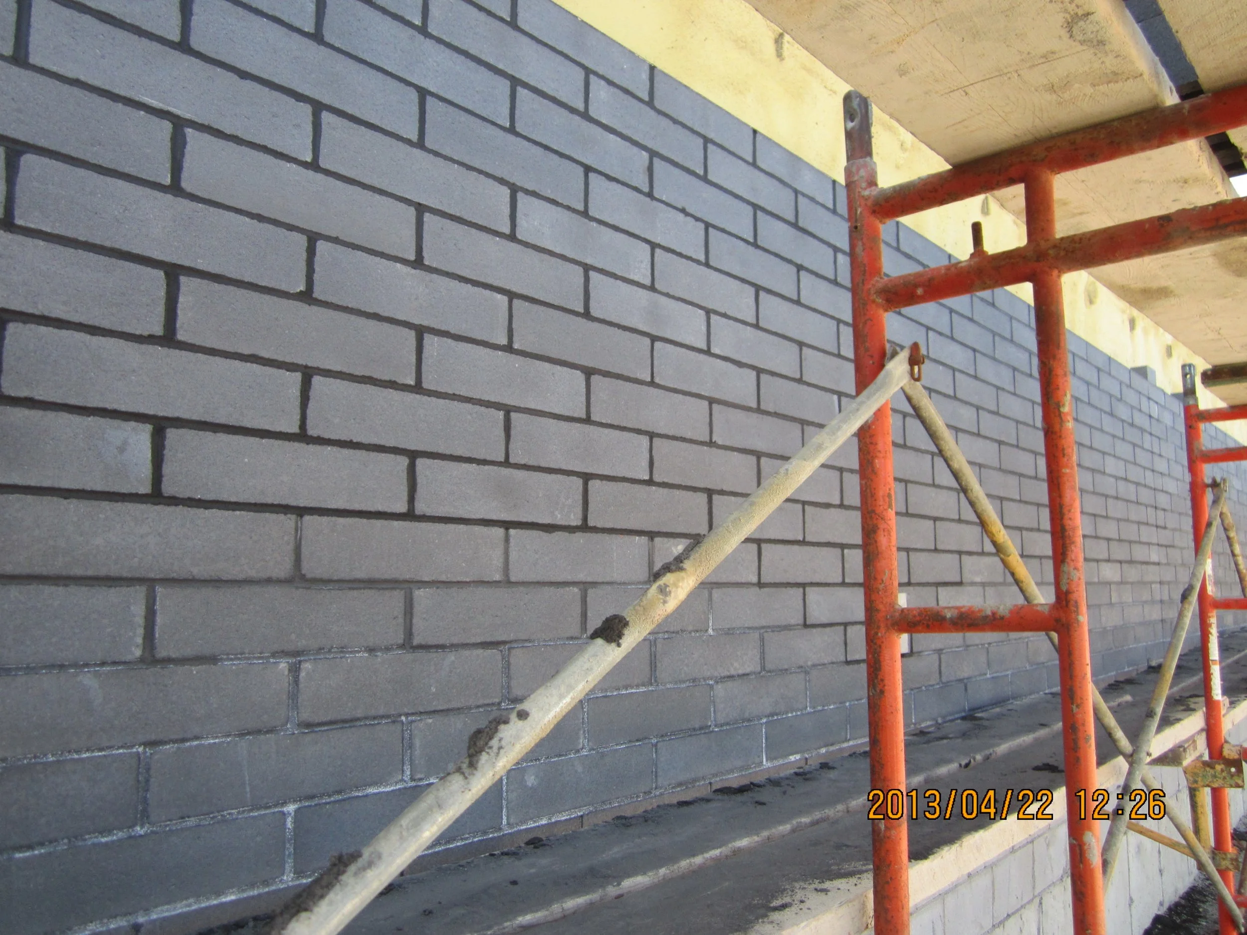 Close-up of a brick wall under construction with red and white scaffolding in place.