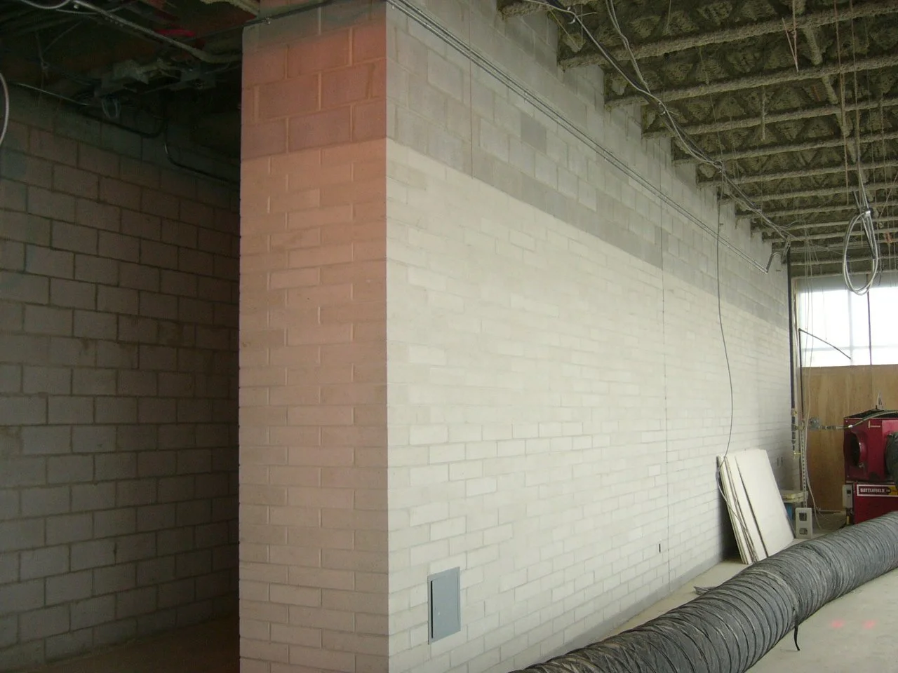 Interior construction site with unfinished walls, exposed ceiling, electrical wiring, and construction equipment.
