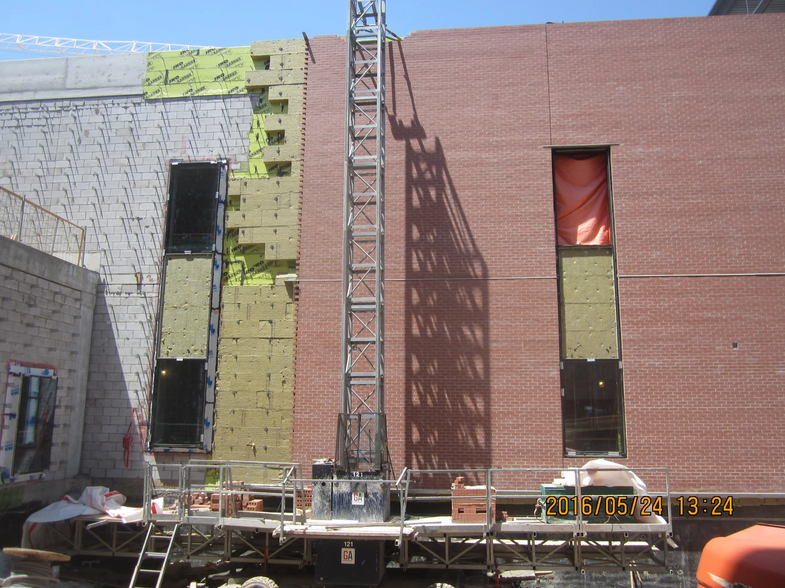 Construction site with brick building under construction, showing open windows and scaffolding, with a crane casting a shadow on the wall. The photo is timestamped May 24, 2016, at 1:24 PM.