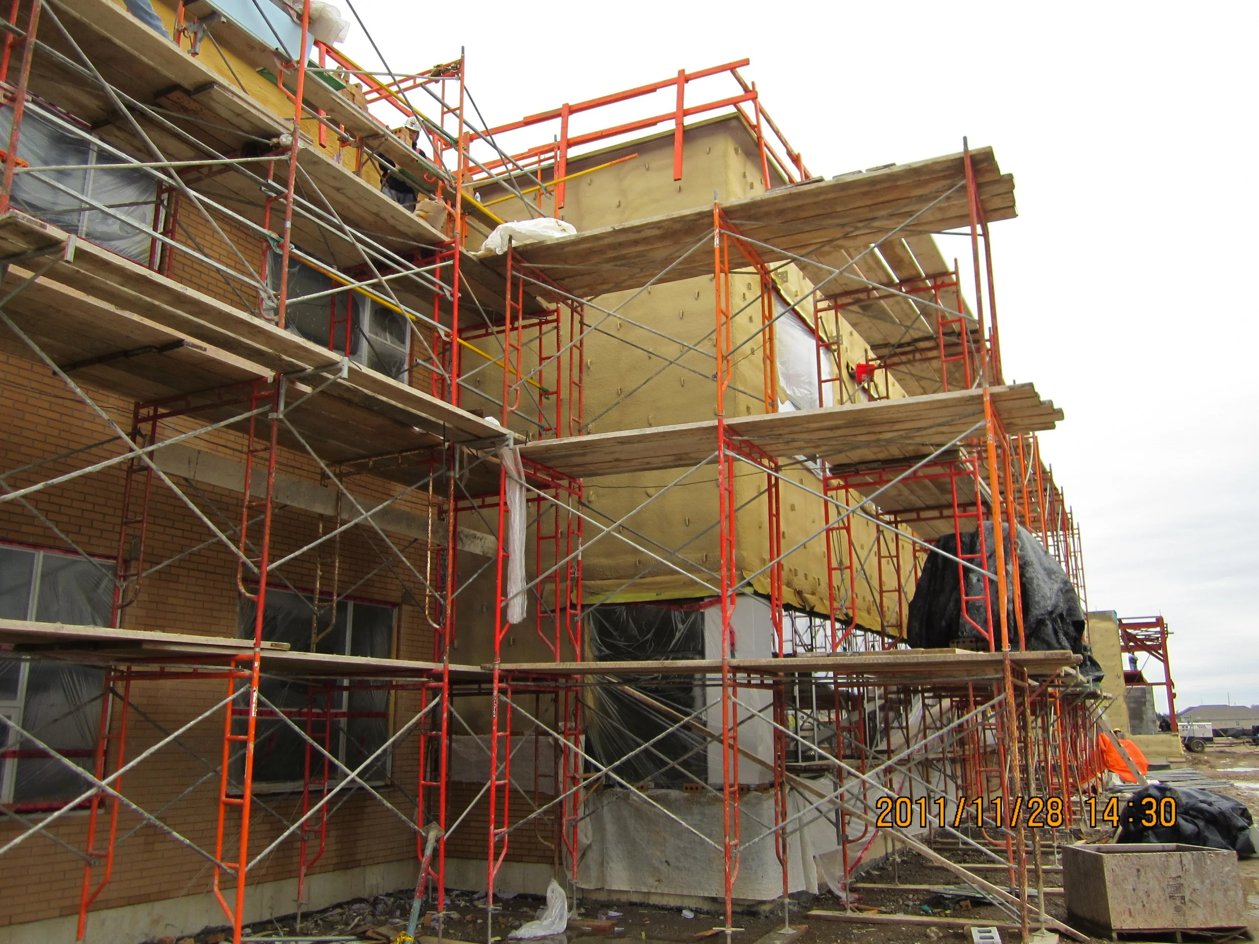 Construction scaffolding surrounds a building with visible brick walls, and workers are likely involved in remodeling or building.