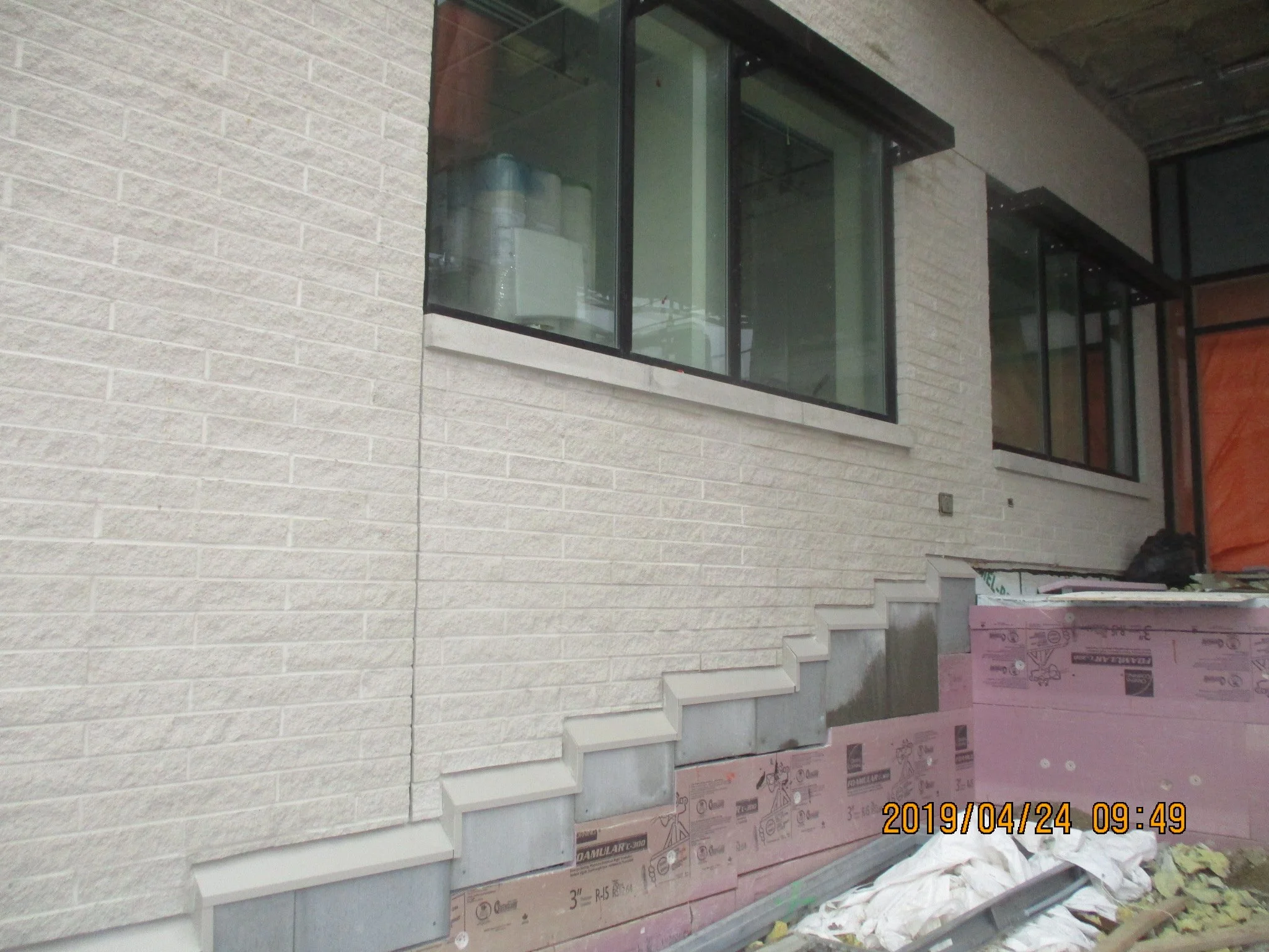 Construction site showing an exterior wall with brick veneer, window frames, and partially installed stair steps.