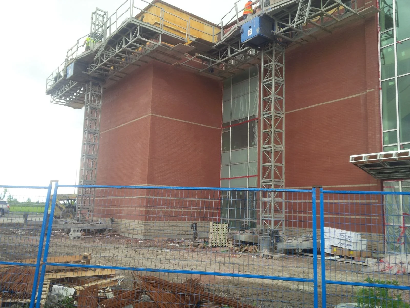 Construction site with a building wrapped in scaffolding and a safety fence in the foreground.