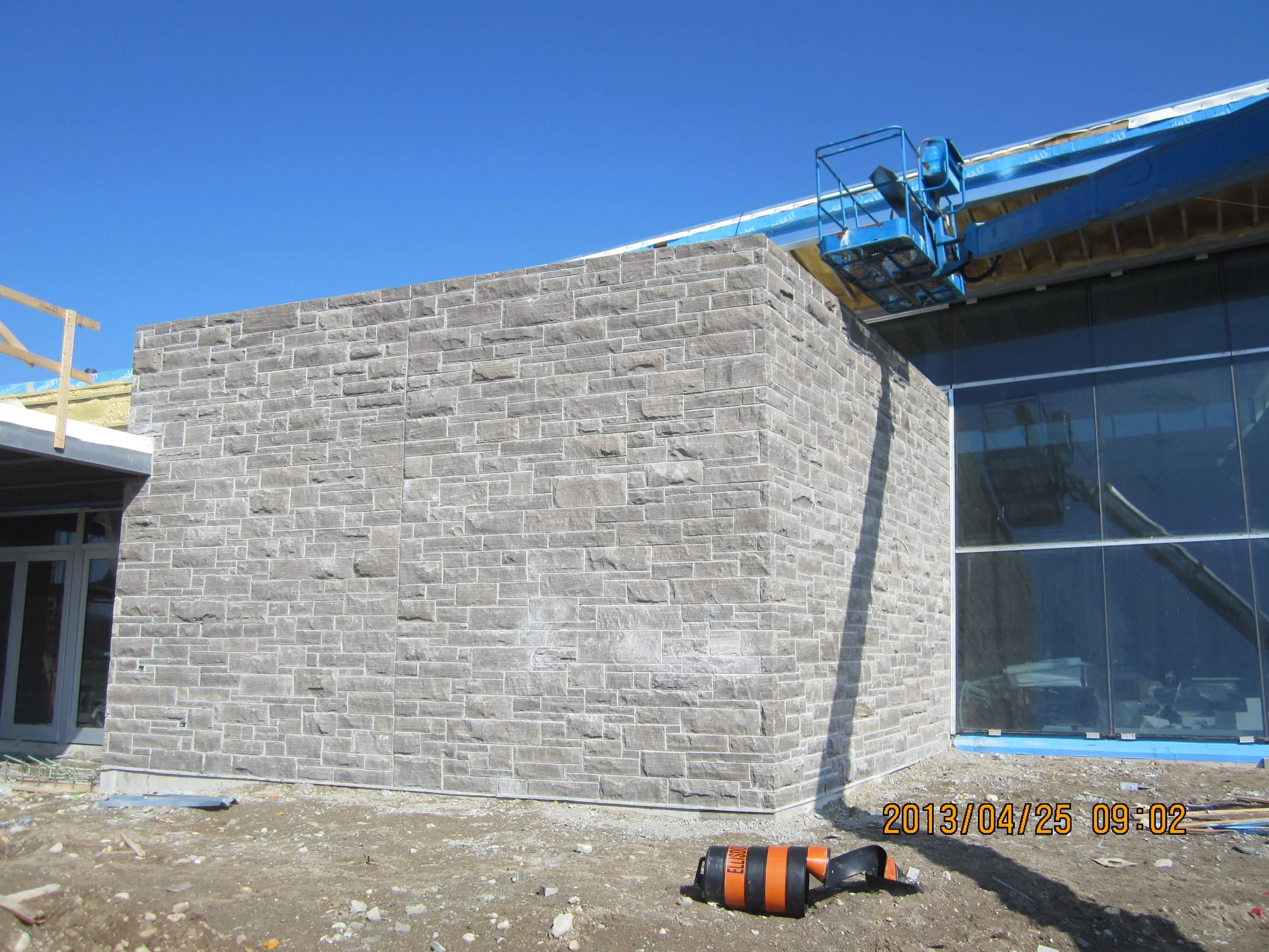 Building under construction with a stone wall, scaffolding, and a blue sky.